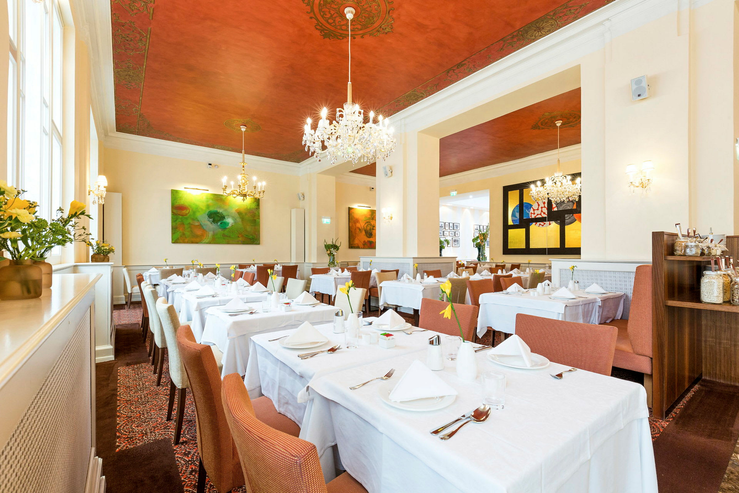 Innredning av en elegant restaurant med hvite duker på bordene, stilige stoler og dekorativt malt tak. (AI-generert tekst)