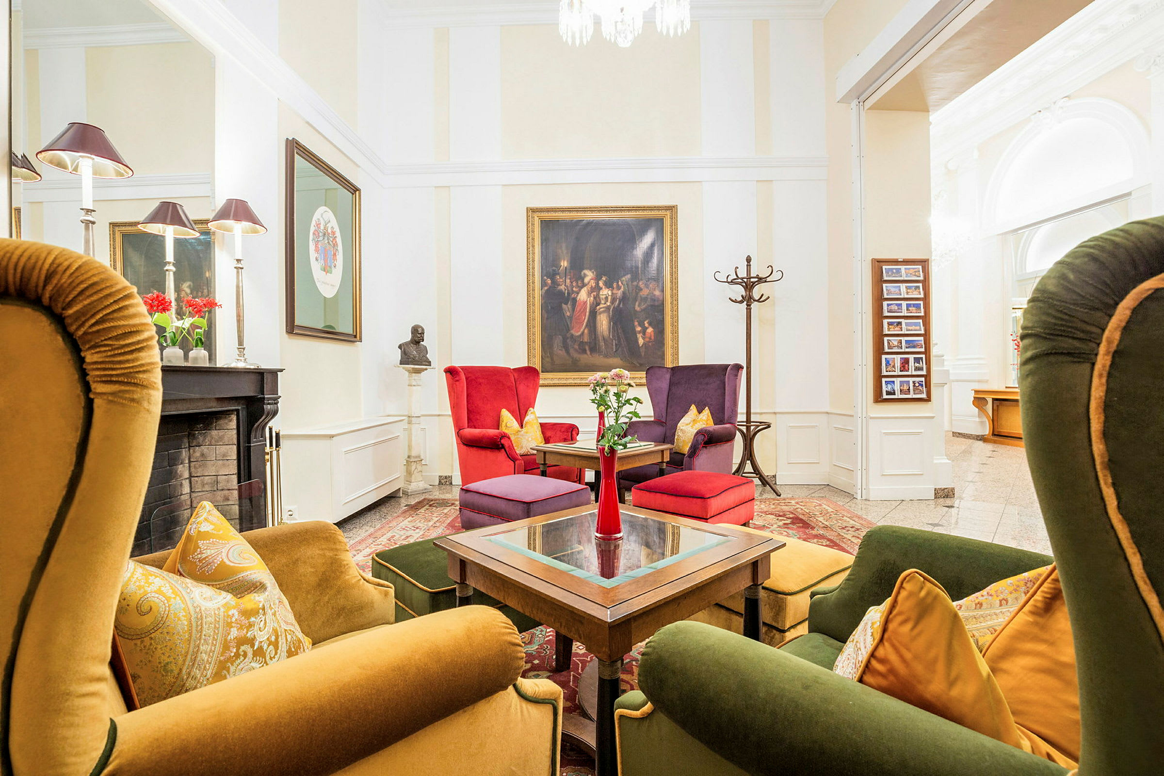 Et stilfullt innredet loungeområde med fargerike lenestoler og sofaer rundt et bord. Veggene er dekorert med kunst, og en peis med dekorasjoner er synlig på siden. (AI-generert tekst)