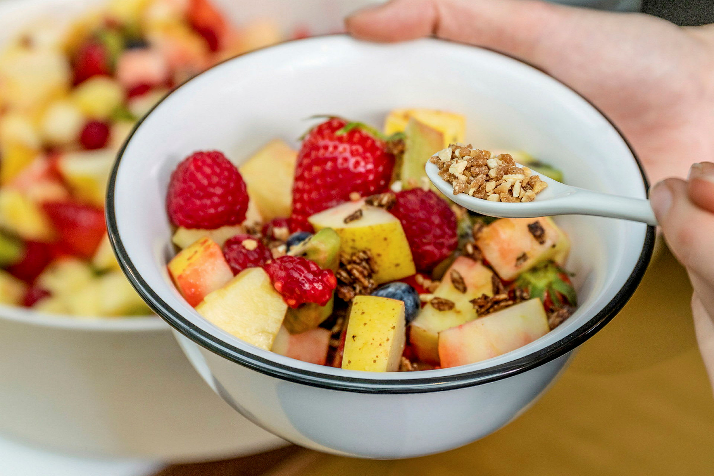 En bolle med fruktsalat som inneholder forskjellige frukter og bær, samt en skje med granola. (AI-generert tekst)