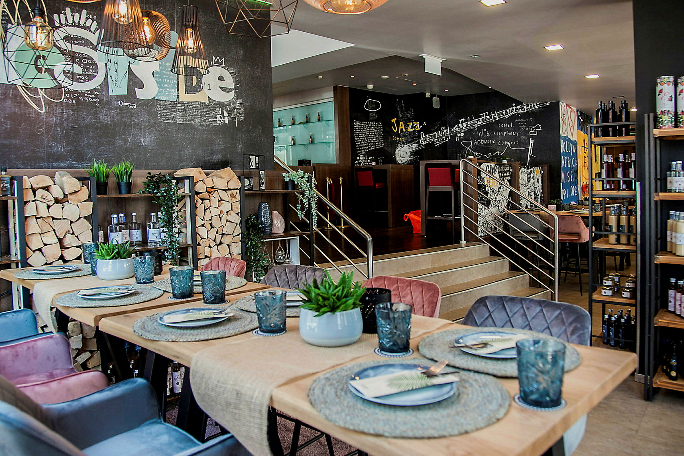 En restaurant eller kafé med moderne interiørdesign. Bordet er dekorert med tallerkener, glass og en liten plante. Veggene har kreative tegninger, og det er trestokker som en del av interiøret. (AI-generert tekst)