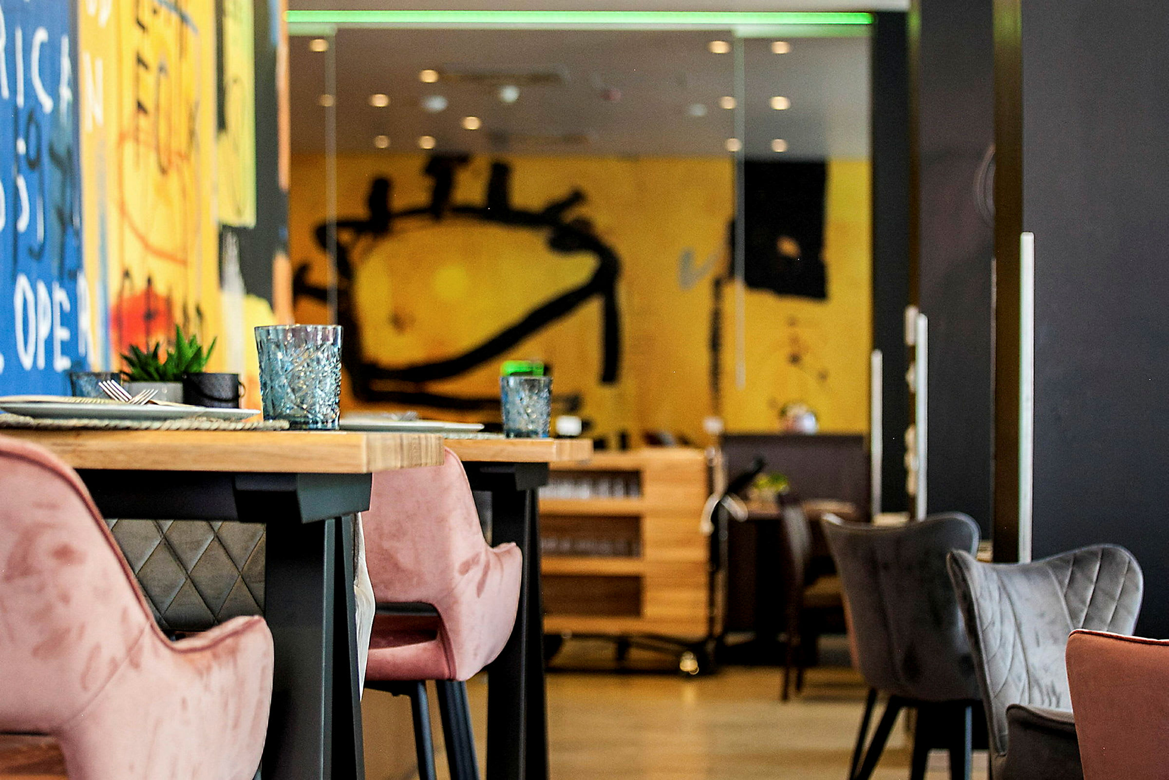 Interiør av en moderne restaurant med fargerike veggmalerier og bord med komfortable stoler. (AI-generert tekst)
