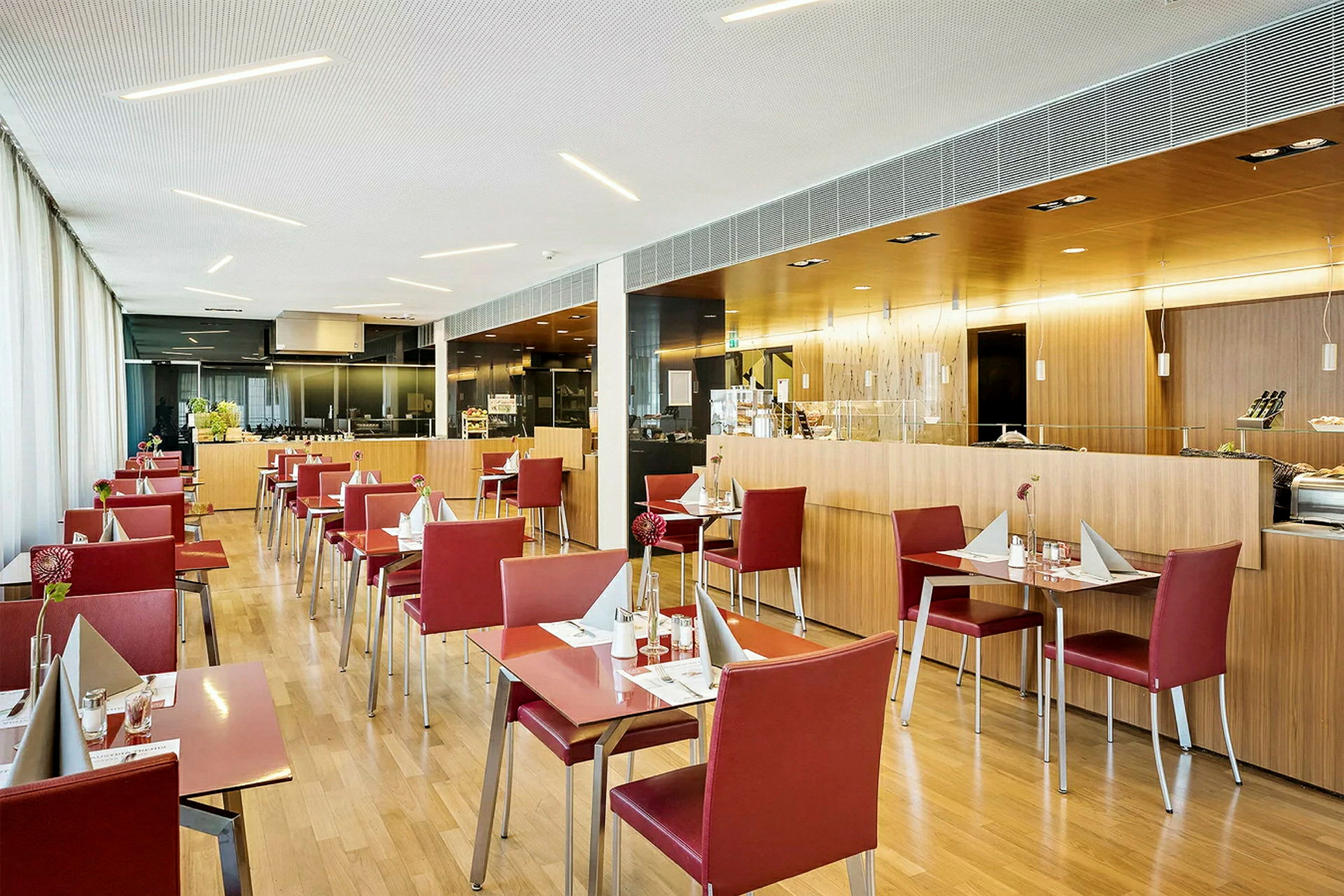 En moderne restaurant med røde stoler og lyse trebord, tydelig organisert med servietter og glass. (AI-generert tekst)