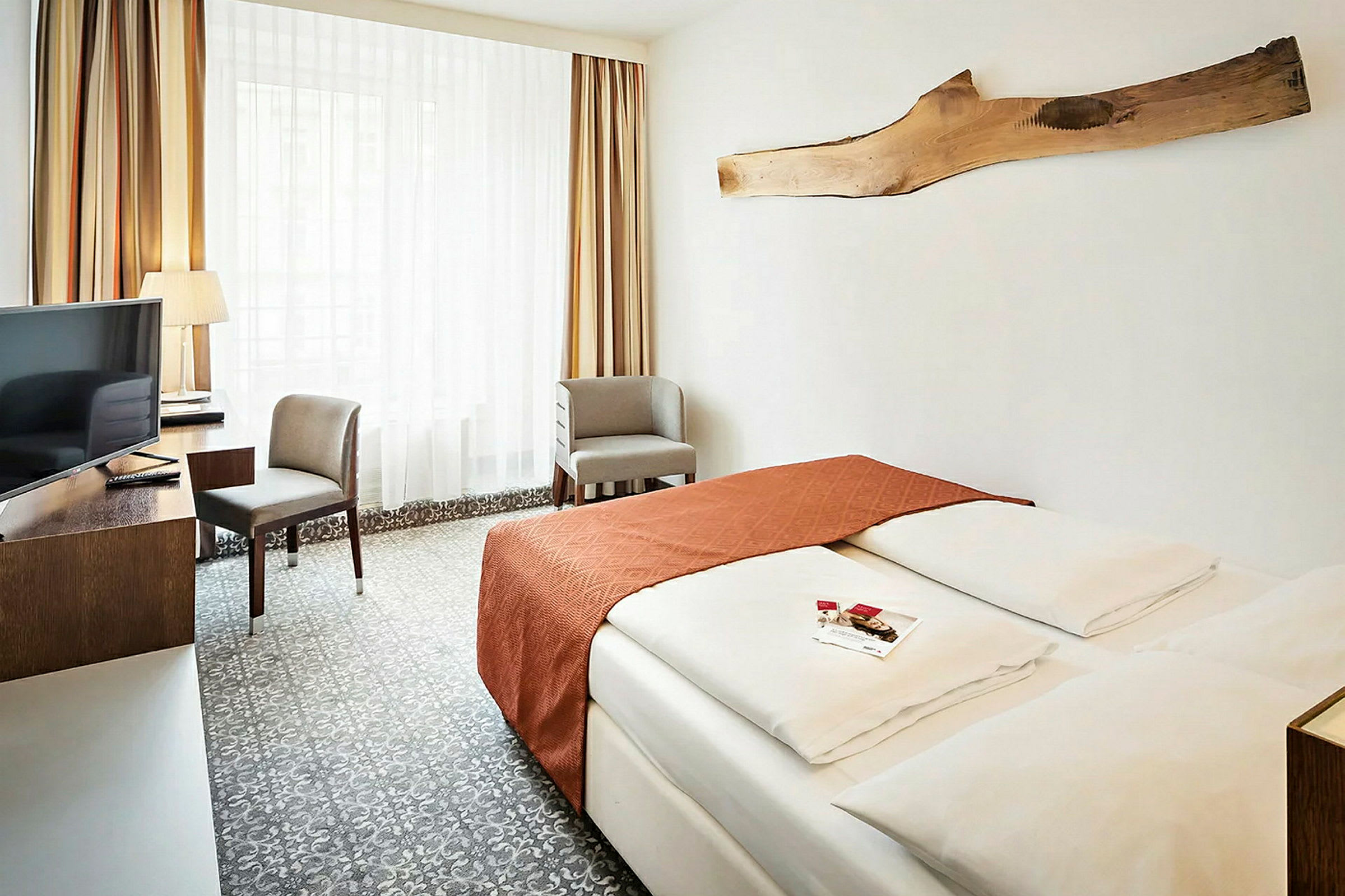 Et hotellrom med en dobbeltseng, et skrivebord med en stol og en TV. Veggene er dekorert med et trestykke. (AI-generert tekst)