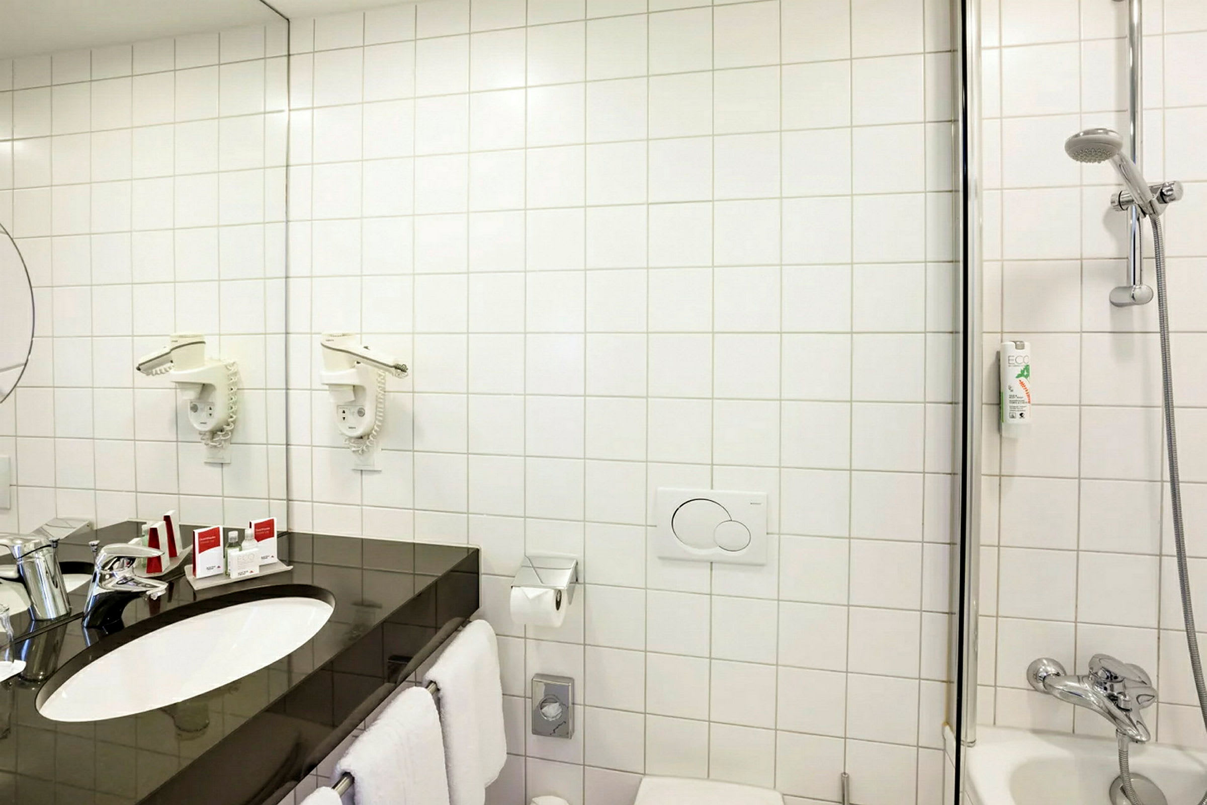 Et badrom med hvite fliser, vask, speil, dusj og toalett. (AI-generert tekst)