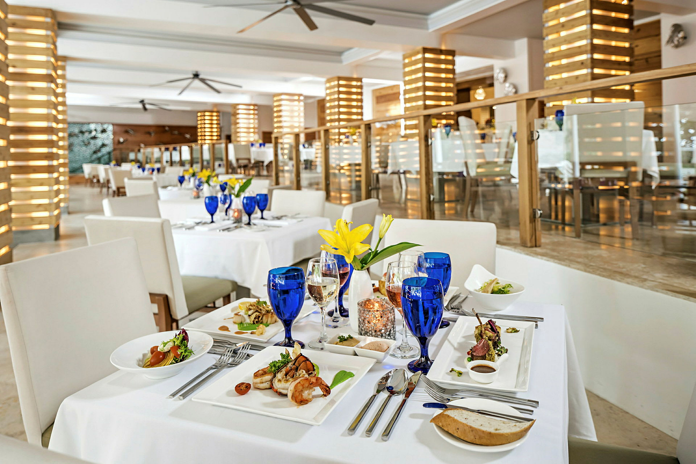 Restaurantbord med hvit duk, blå glass og fat med mat. (AI-generert tekst)