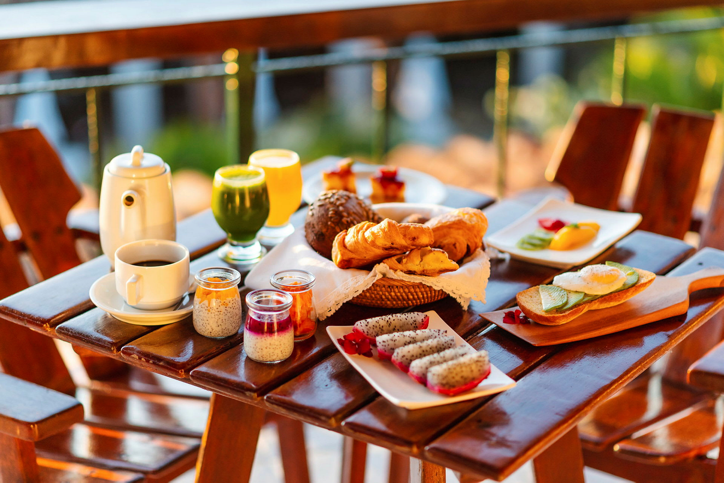 En frokost med en rekke retter som serveres på et bord utendørs, inkludert brød, croissanter, fersk frukt, juice og kaffe. (AI-generert tekst)