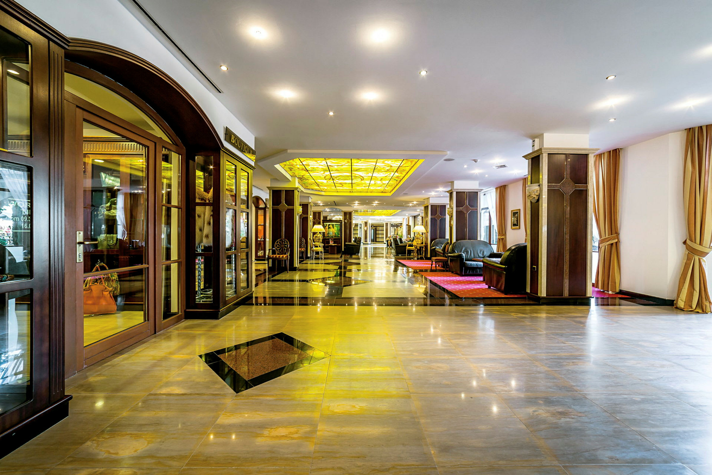 En elegant hotellobby med skinnende gulv, komfortable sofaer og et gult glasstak. (AI-generert tekst)