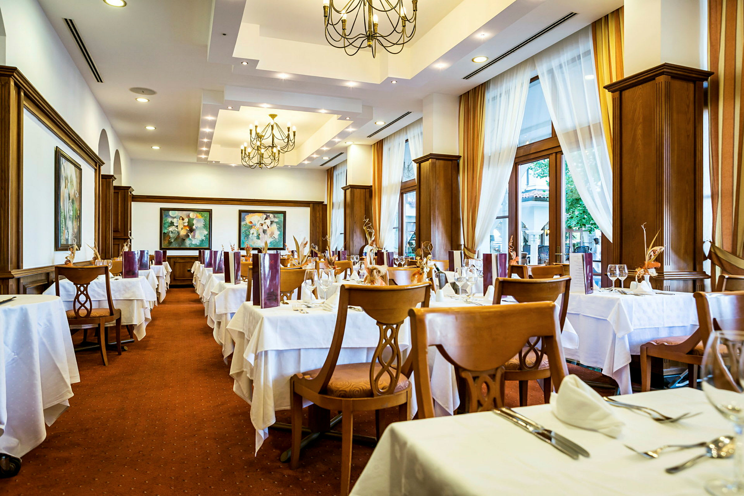 Interiør av en restaurant med dekkede bord og stoler, lyse gardiner og dekorative taklamper. (AI-generert tekst)