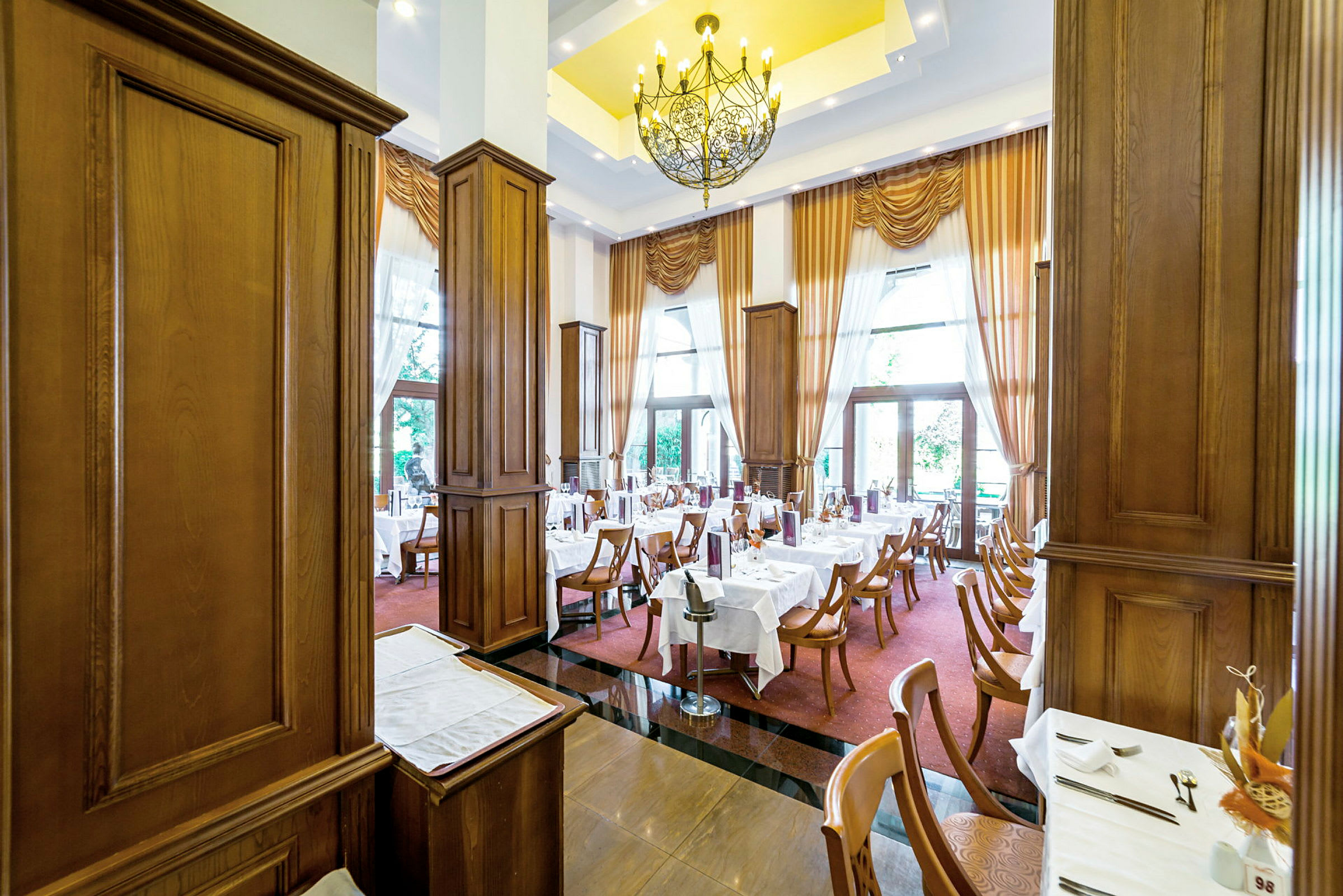En elegant restaurant med dekkede bord, trepaneler og store vinduer med gardiner. (AI-generert tekst)