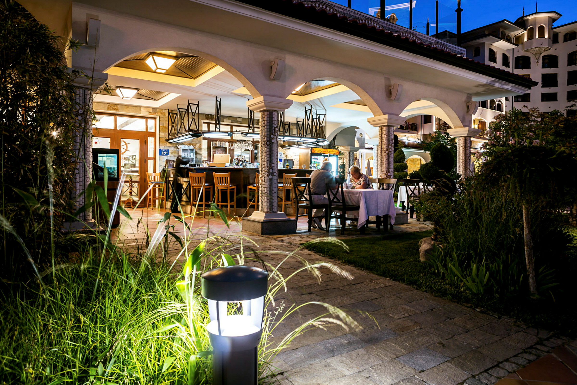 Bilde av en restaurant med buet arkitektur, utendørsbelysning og en elegant atmosfære om kvelden. (AI-generert tekst)