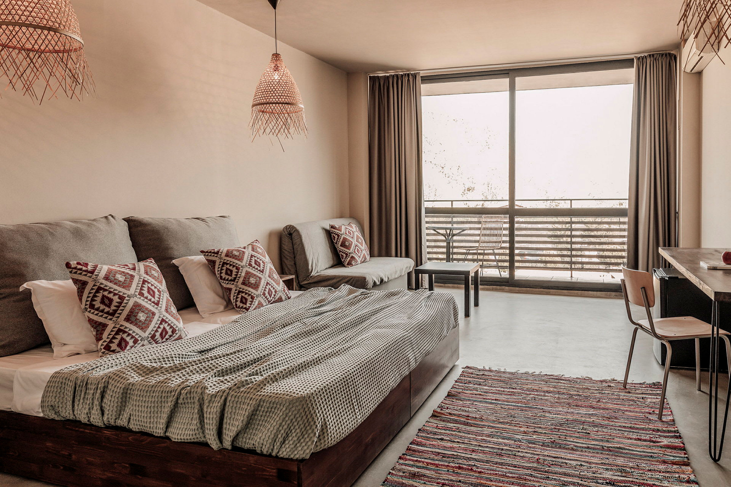 Et lyst og moderne hotellrom med seng, sofa og en balkong med utemøbler. (AI-generert tekst)