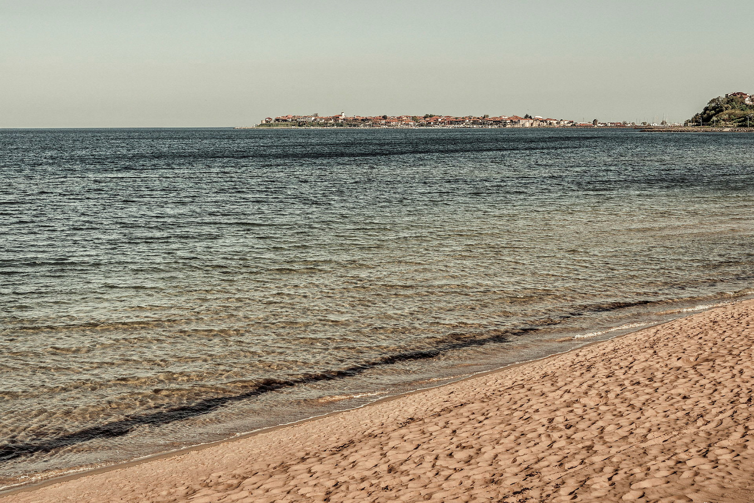 Bilde av en sandstrand ved havet med en by i bakgrunnen. (AI-generert tekst)