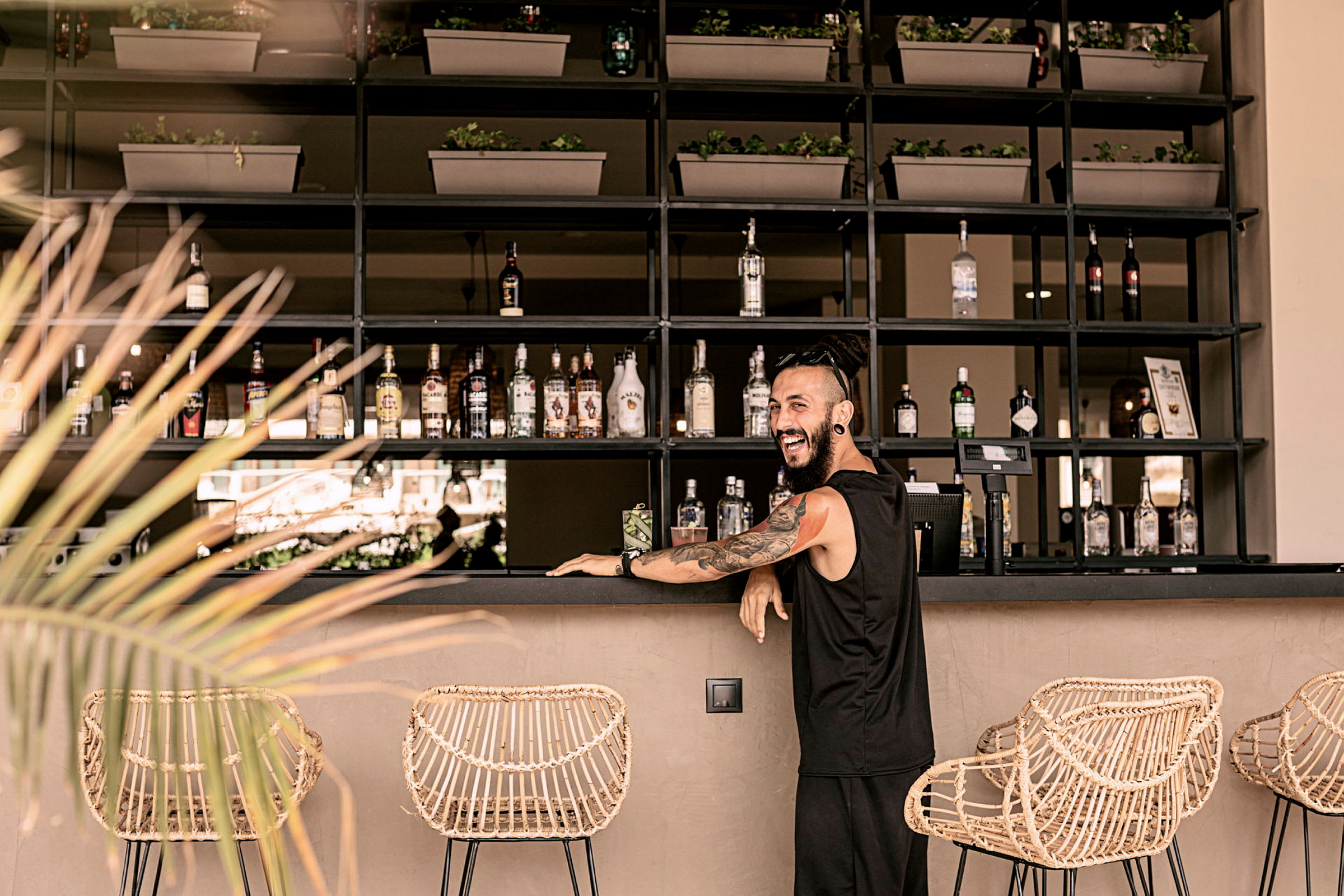 En elegant bar med flasker, kurvstoler og plantepynt. (AI-generert tekst)