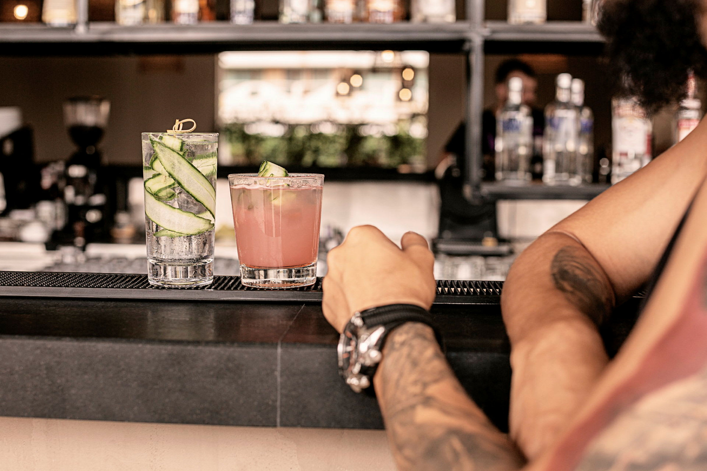 To cocktails på en bardisk, med en persons arm i forgrunnen. (AI-generert tekst)