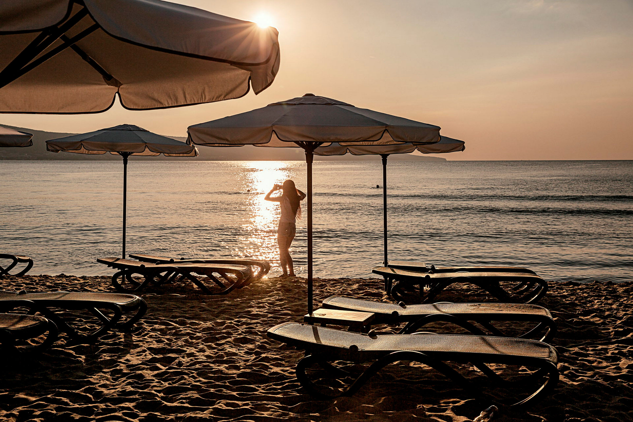 Solstoler og parasoller på en sandstrand ved solnedgang. (AI-generert tekst)