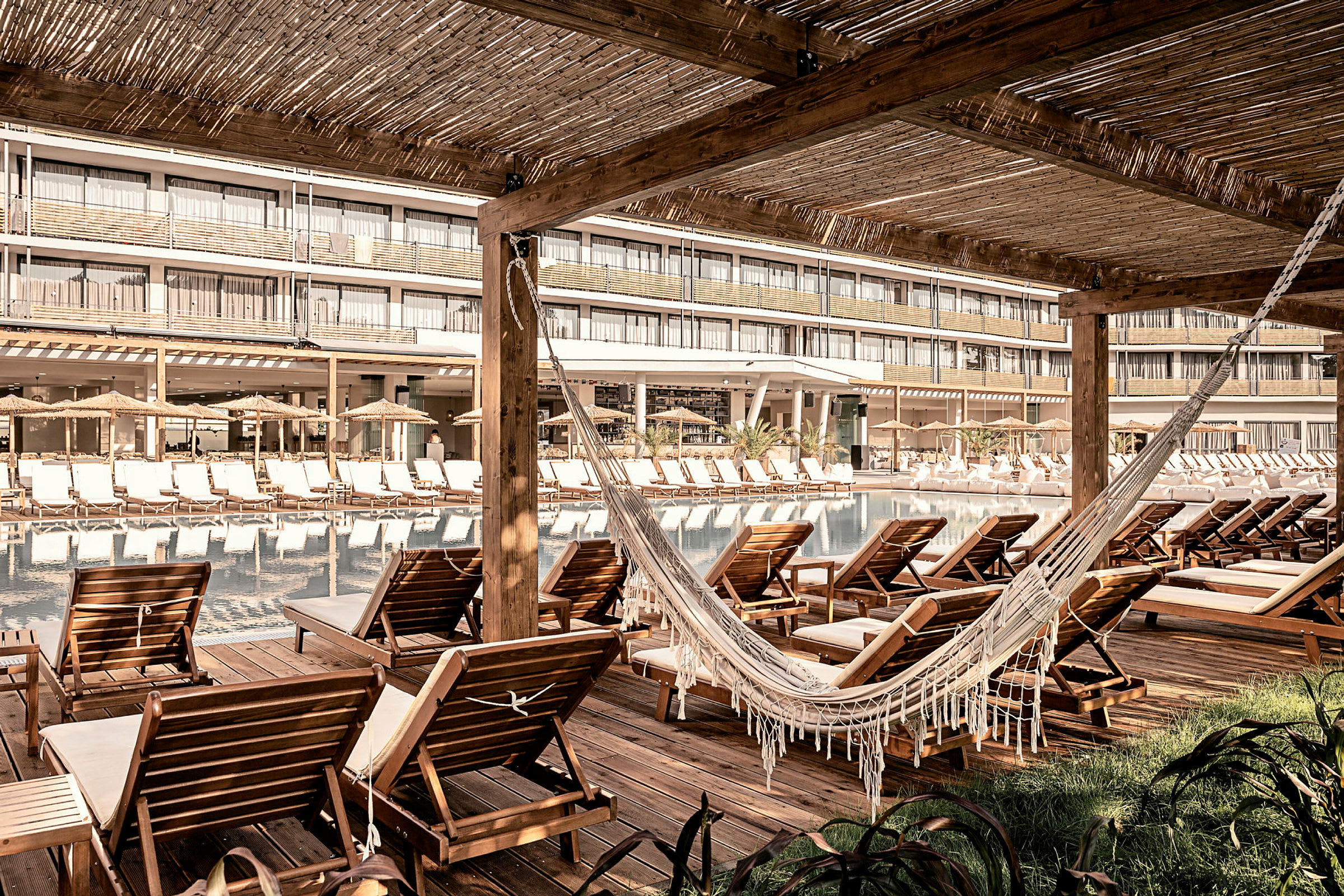 Stoler og en hengekøye ved et basseng, med hotellbygningen i bakgrunnen. (AI-generert tekst)