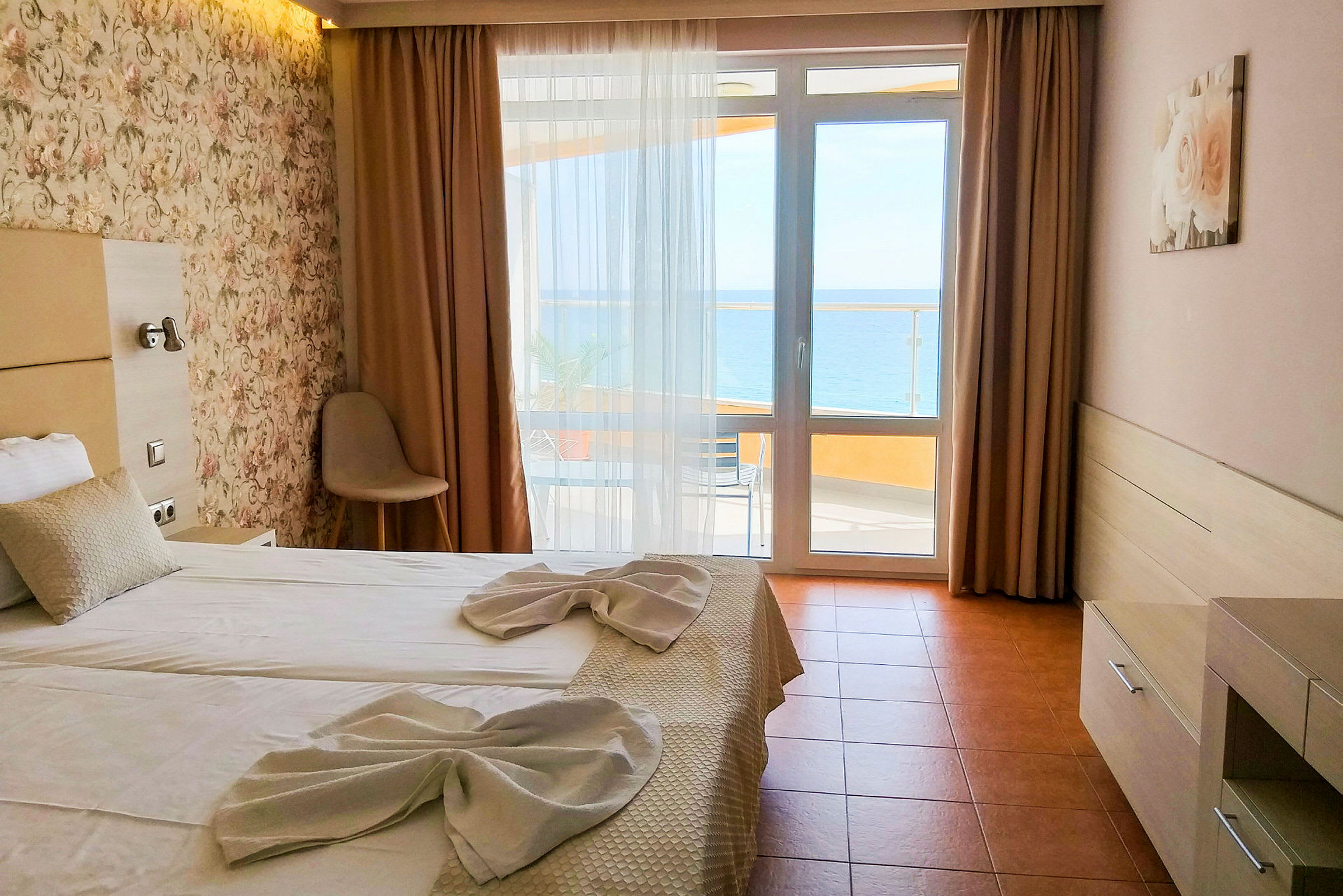 Et hotellrom med en dobbeltseng oppredd med hvite laken og dekorert med håndklær. Det er et vindu med utsikt mot havet. (AI-generert tekst)