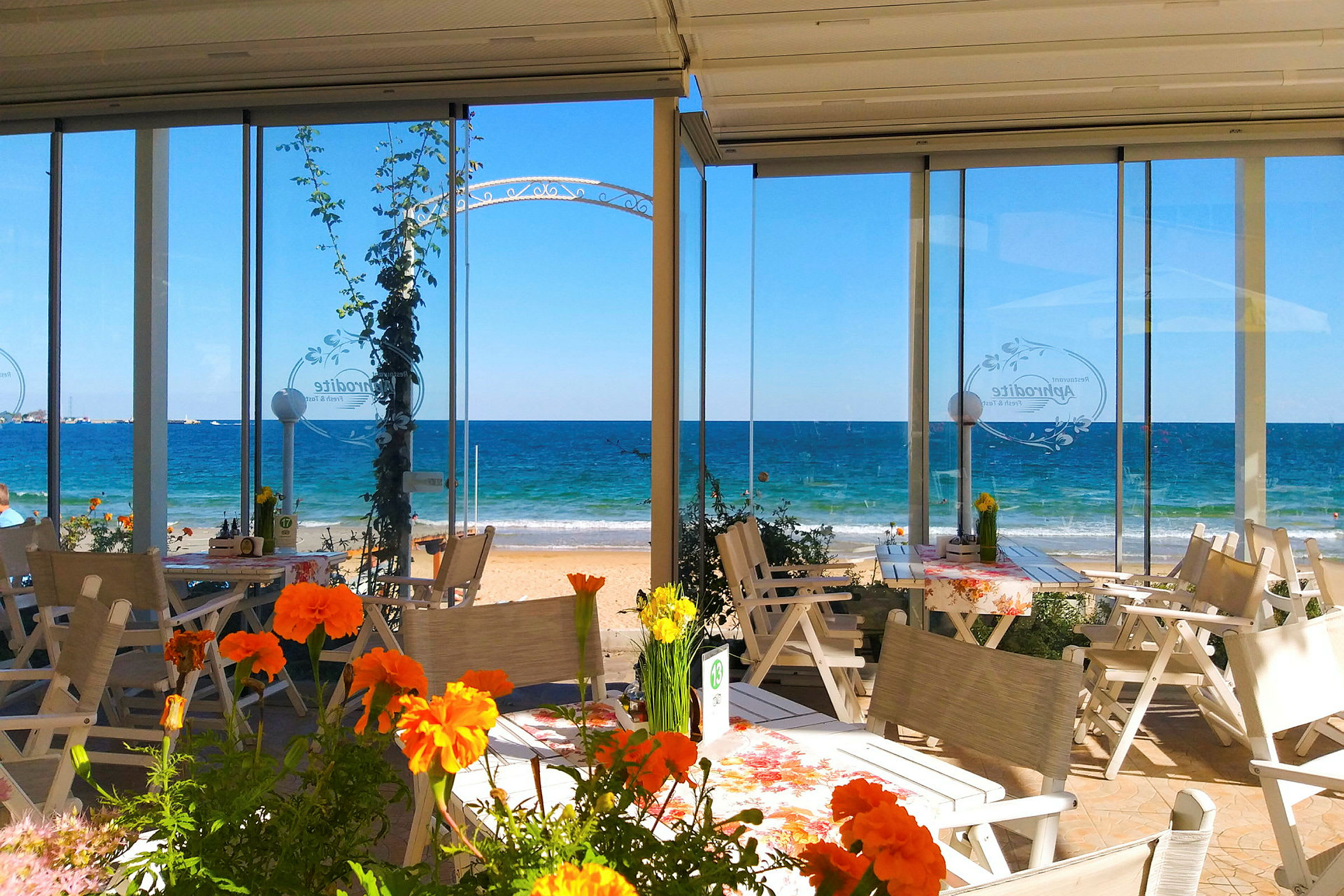 Utendørs serveringsområde med blomster og utsikt mot havet. (AI-generert tekst)