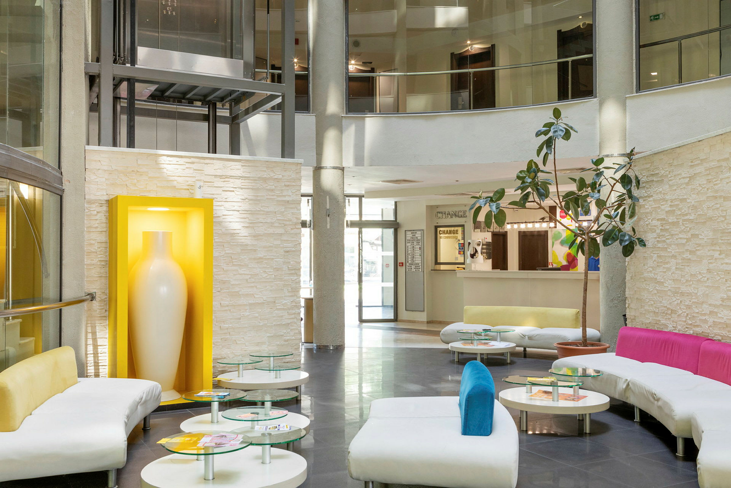 En moderne hotellobby med sofaer, glassbord og en stor hvit vase i en gul ramme. (AI-generert tekst)