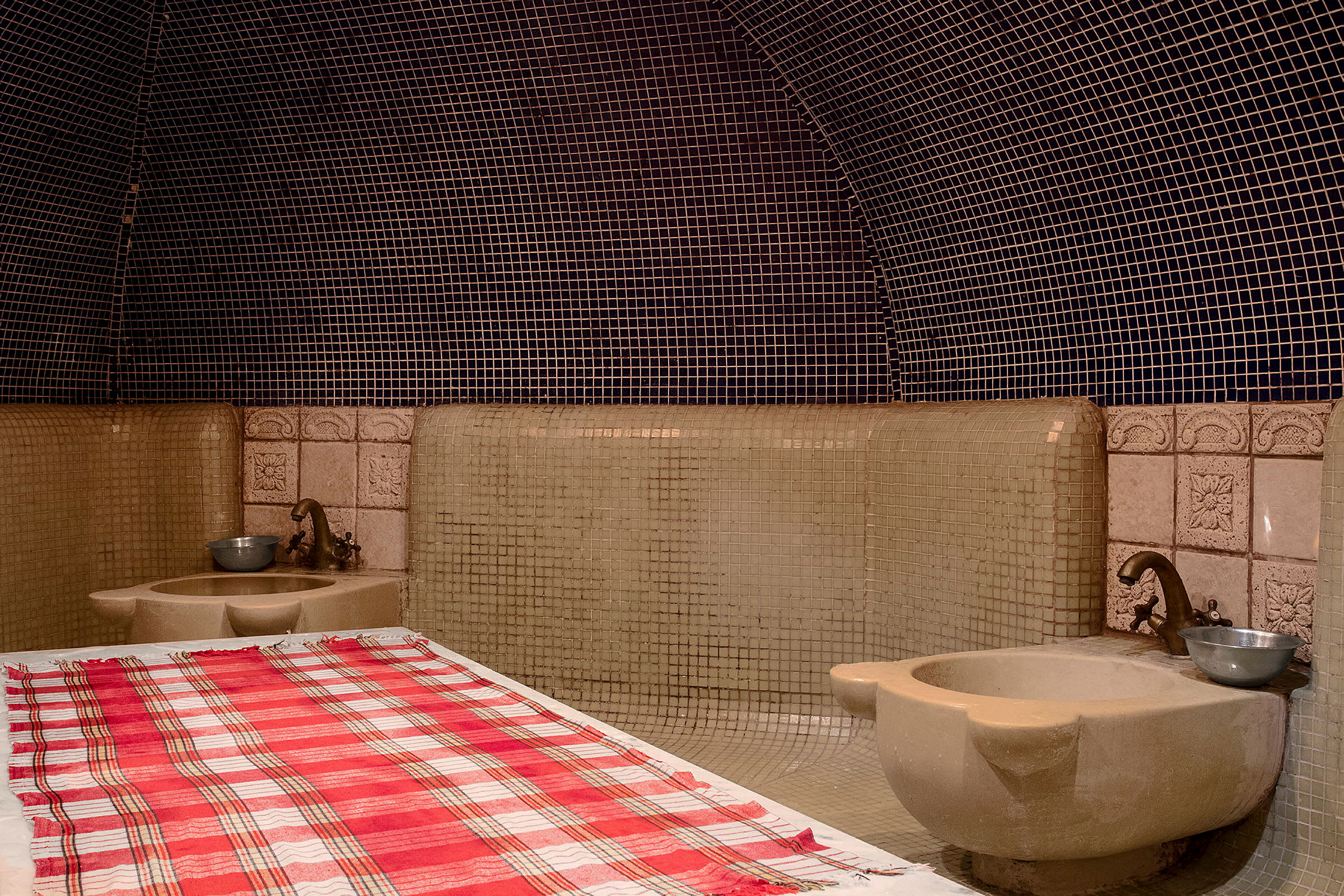 Et tradisjonelt hamam-rom med flislagte vegger og en benk dekket med et rutete håndkle. (AI-generert tekst)