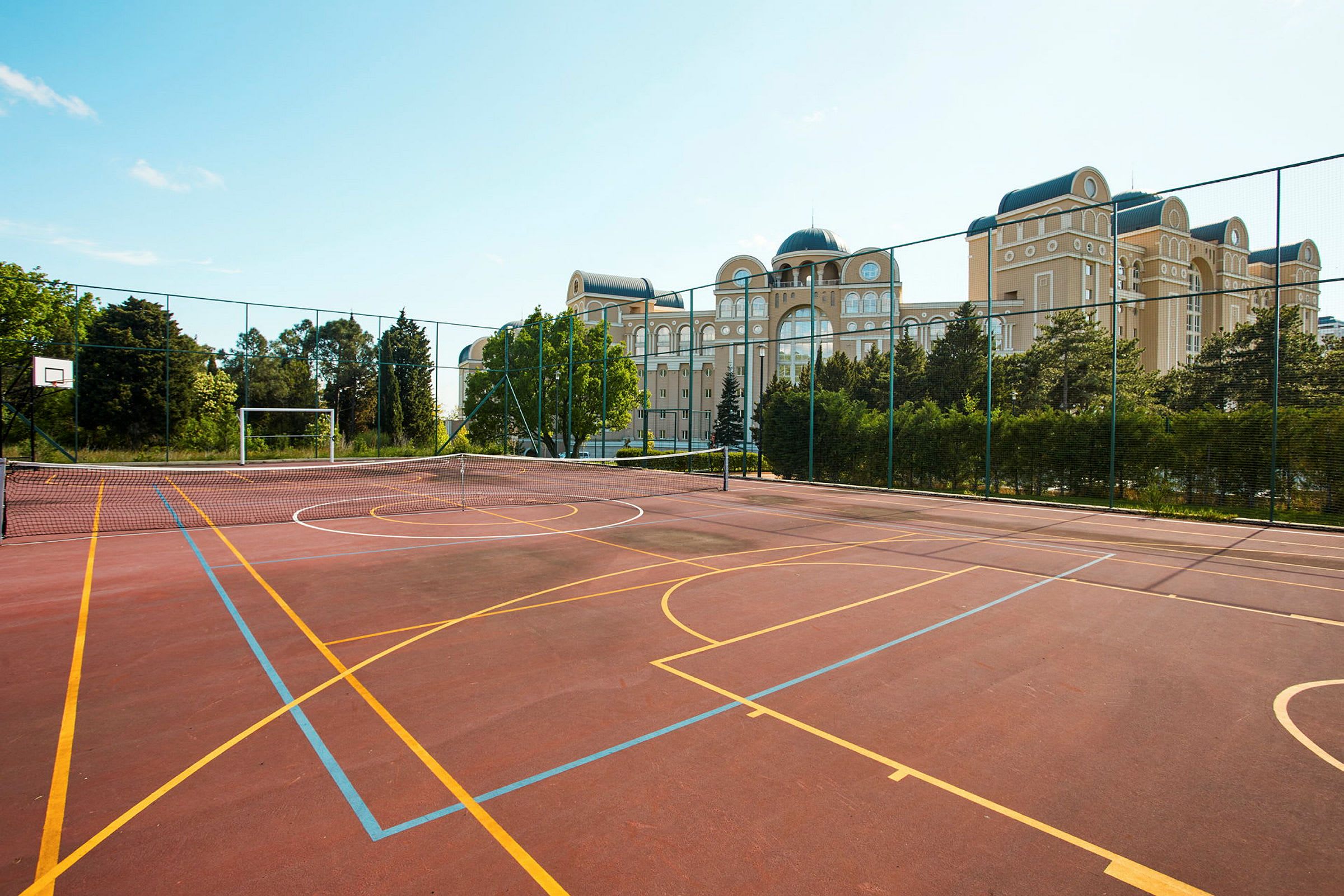En idrettsplass med basketballkurv og målbur. I bakgrunnen vises bygninger og vegetasjon. (AI-generert tekst)