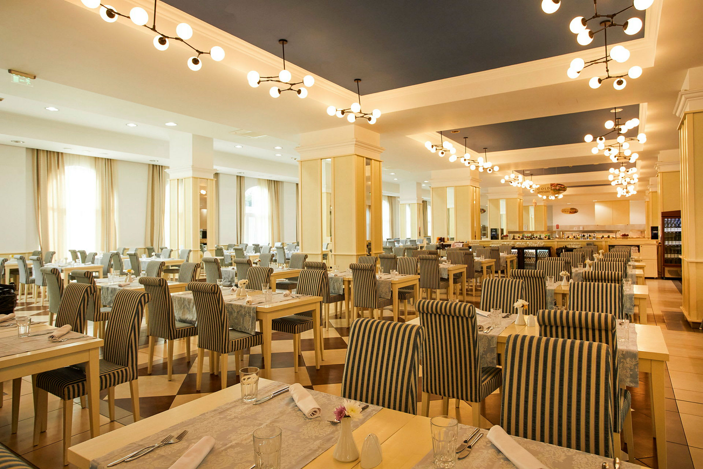 En romslig restaurant med bord og stoler i stripete stoff og taklamper i moderne design. (AI-generert tekst)