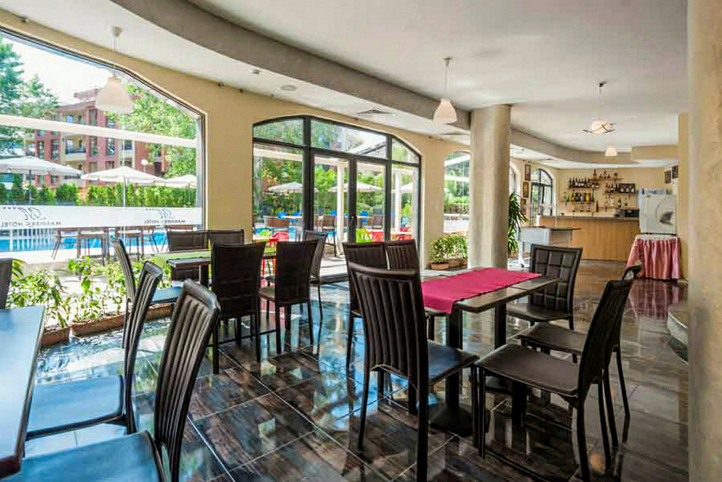 Restaurant med bord og stoler, store vinduer vender mot uteområdet. (AI-generert tekst)