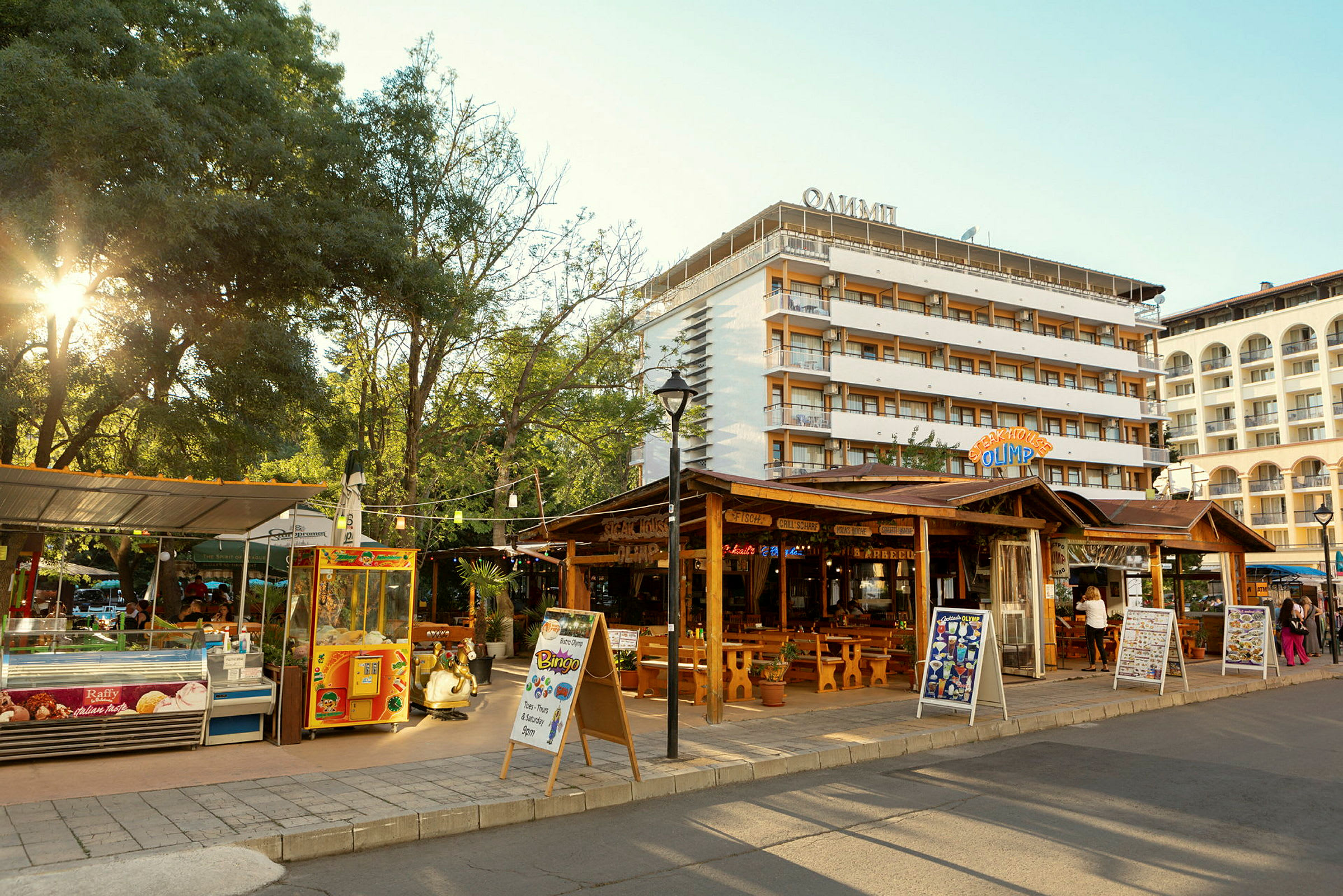 En gate med restauranter og butikker, samt hotellbygninger i bakgrunnen. (AI-generert tekst)