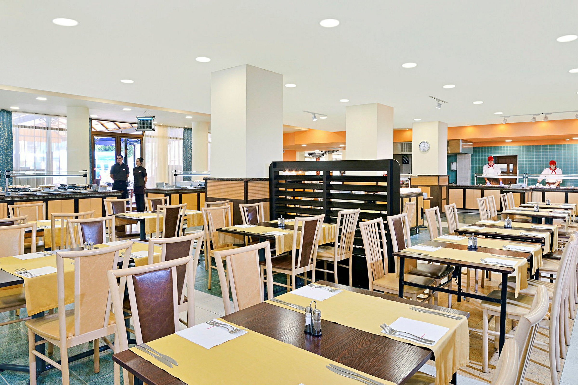 Restaurant med oppstilte bord og stoler, ferdig dekket for gjester, i en lys og romslig spisesal. (AI-generert tekst)