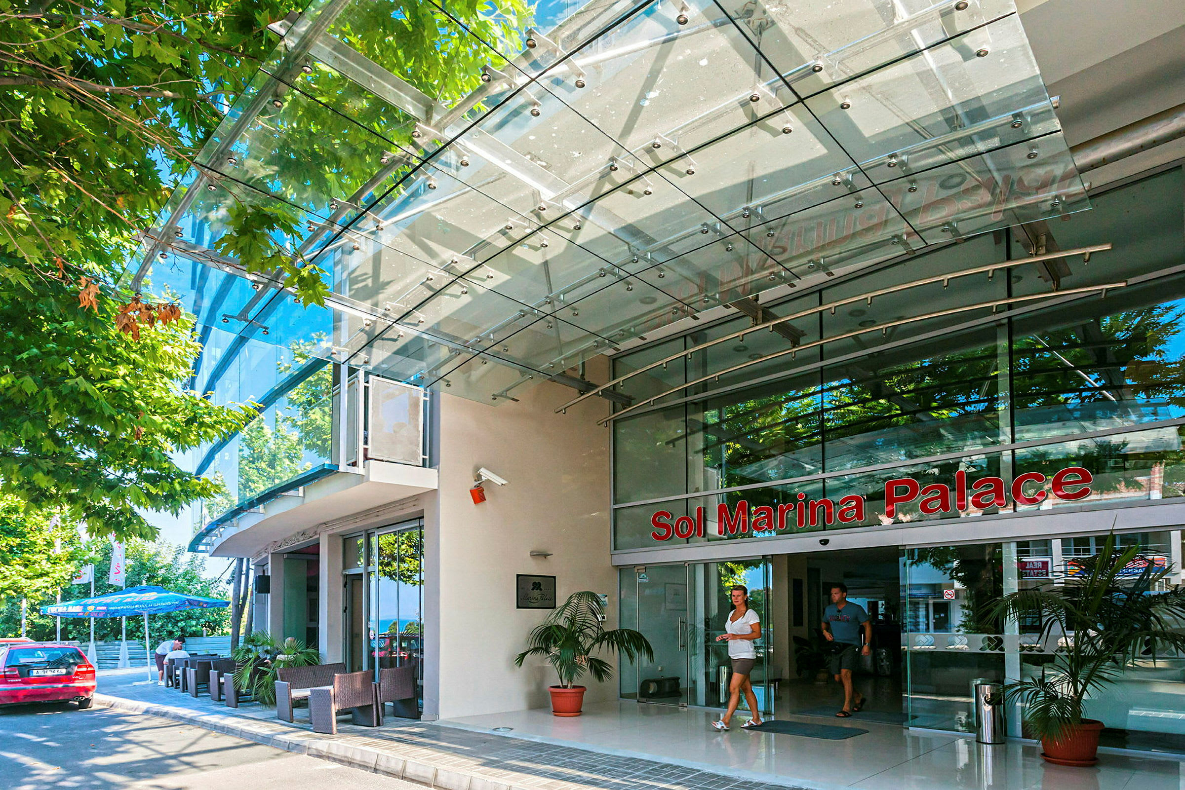 Inngangen til Sol Marina Palace med glassfasade og et skilt med navnet. (AI-generert tekst)