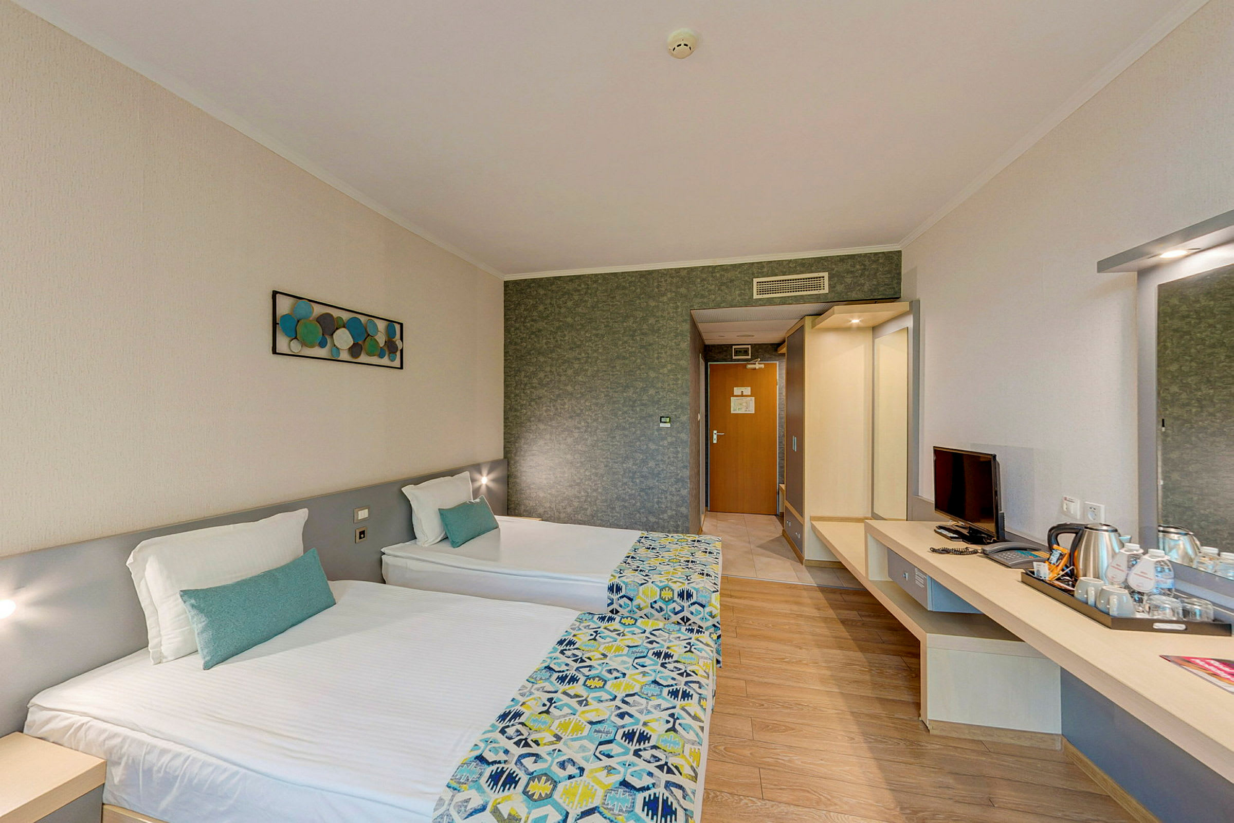 Et hotellrom med to enkeltsenger, et skrivebord med TV og en vannkoker. Et kunstverk henger på veggen. (AI-generert tekst)