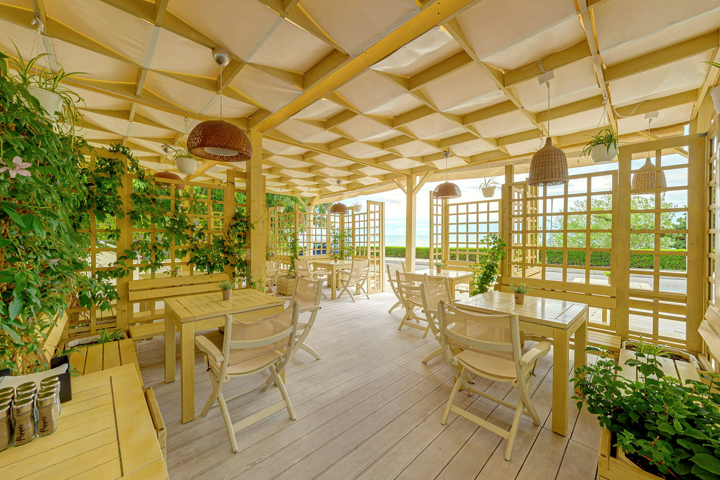 En overbygd treterrasse med bord og stoler, dekorert med planter og trematerialer. (AI-generert tekst)