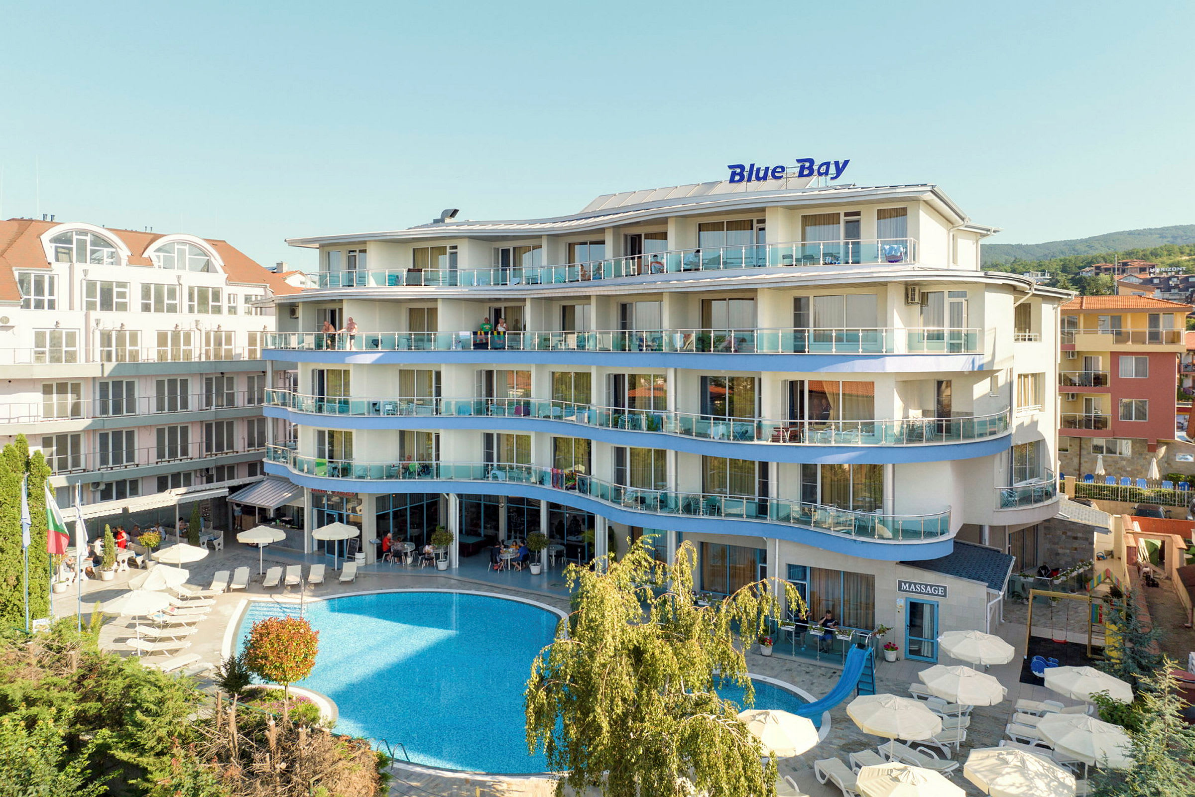 Hotell med basseng foran bygningen og solsenger rundt. (AI-generert tekst)