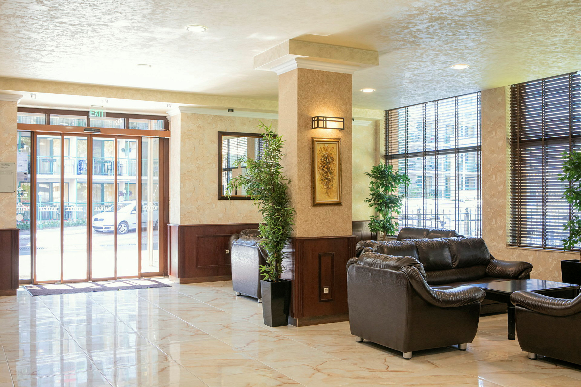 Lys hotellobby med skinnsofaer og en glassinngang. (AI-generert tekst)
