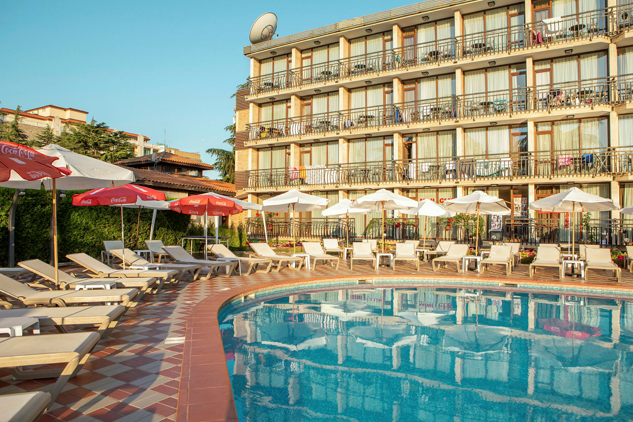 Bilde av et hotellbasseng med solsenger og parasoller, samt hotellbygning i bakgrunnen. (AI-generert tekst)