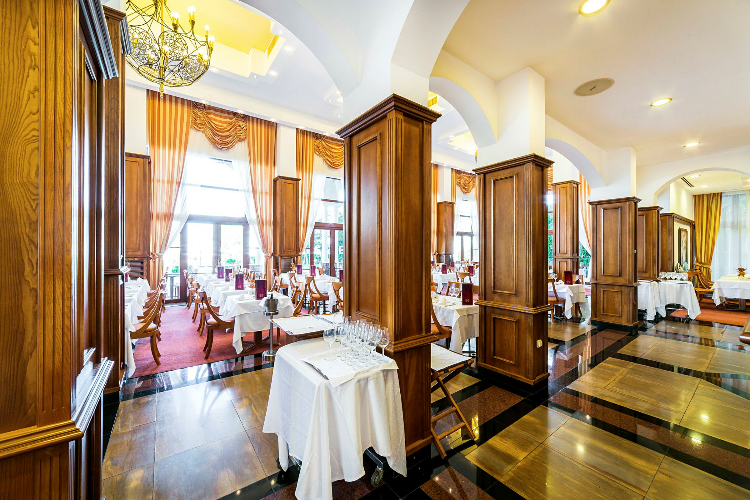 En elegant restaurant med dekkede bord, mørke tregulv og store vinduer med gardiner. (AI-generert tekst)