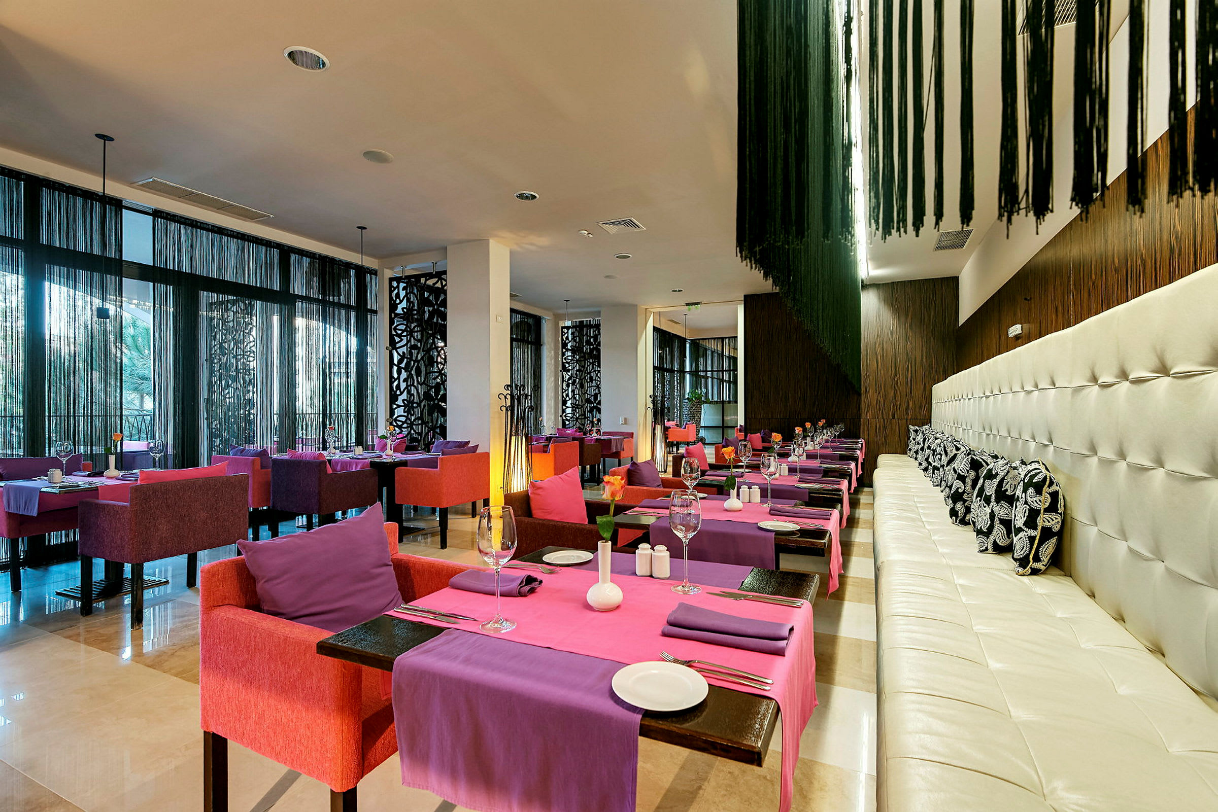 Et moderne innredet restaurantområde med fargerike stoler og bord kledd i lilla og rosa duker. (AI-generert tekst)