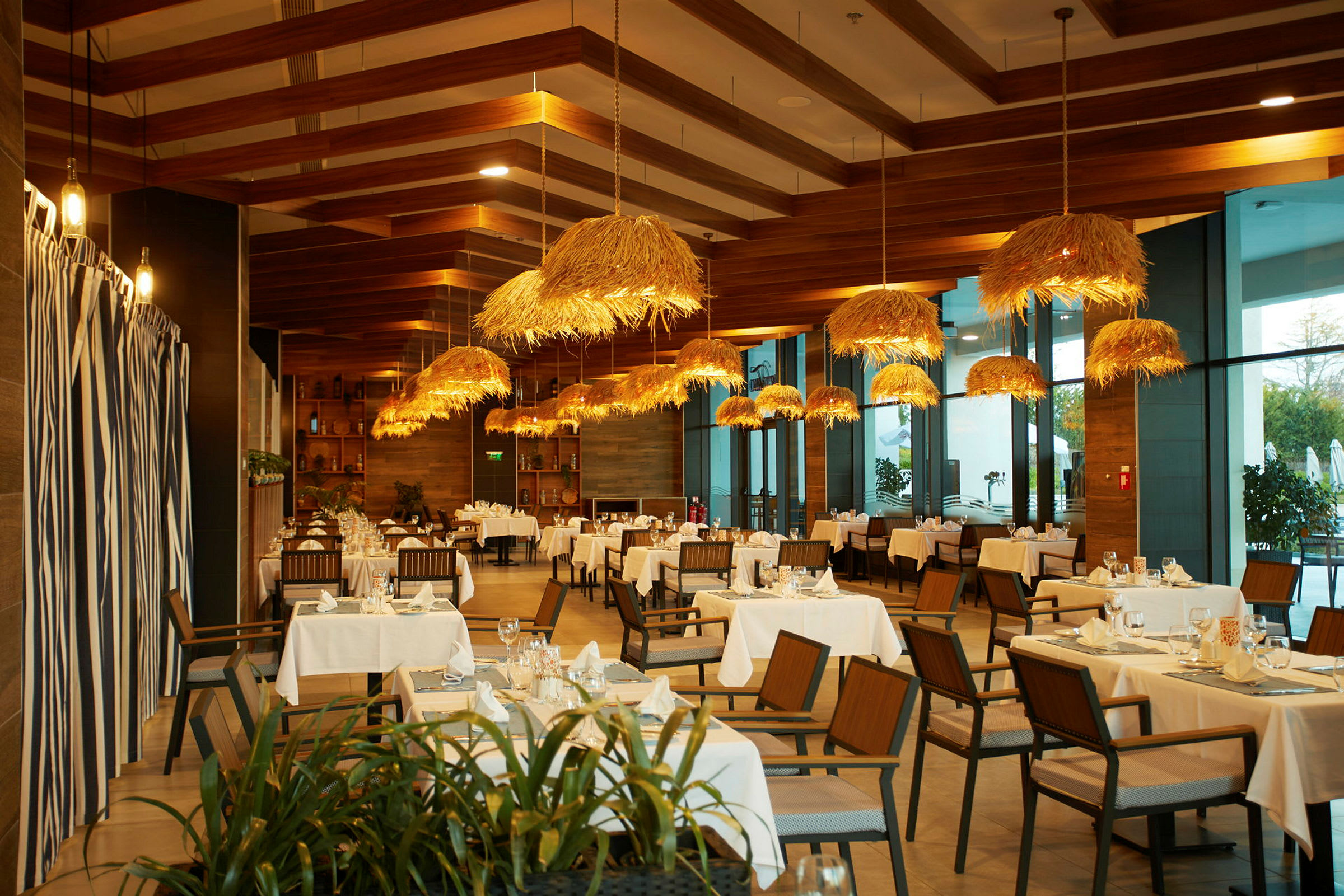 Restaurant med bord, trestoler og hengende lamper med halmdekor. (AI-generert tekst)
