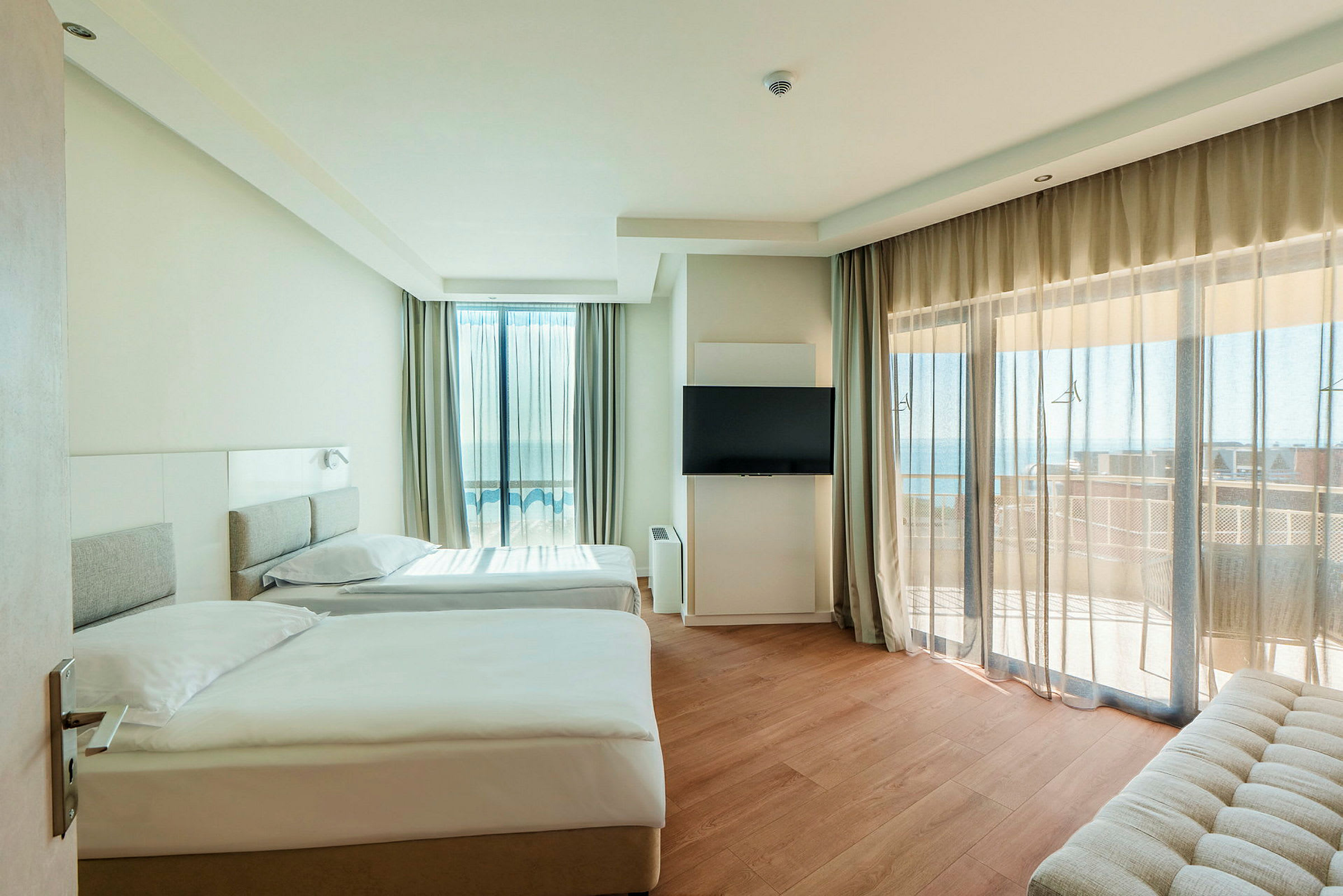 Moderne hotellrom med to enkeltsenger, flatskjerm-TV og balkong med havutsikt. (AI-generert tekst)