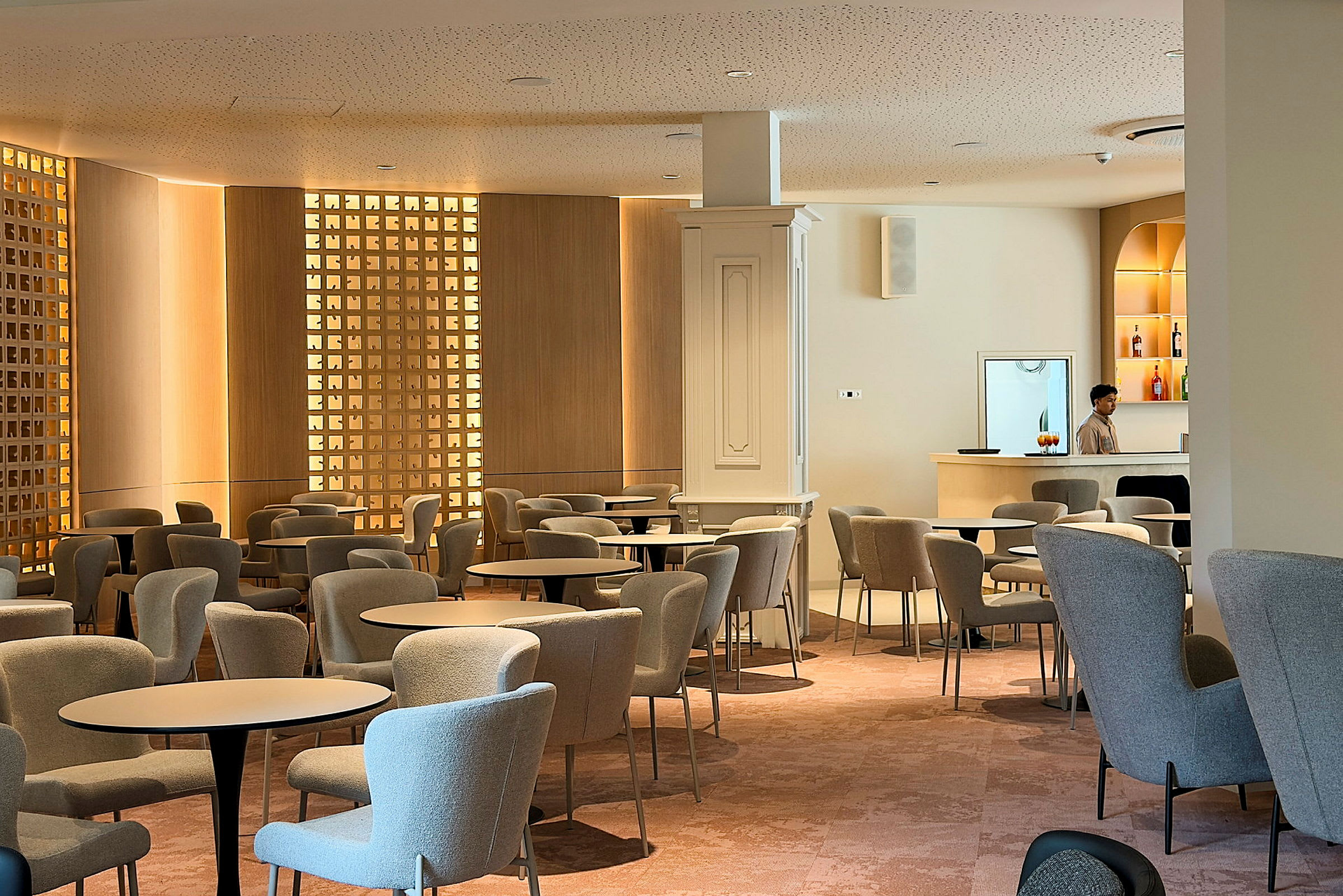 En moderne lounge med komfortable stoler og bord. En person står ved en minimalistisk bardisk. (AI-generert tekst)