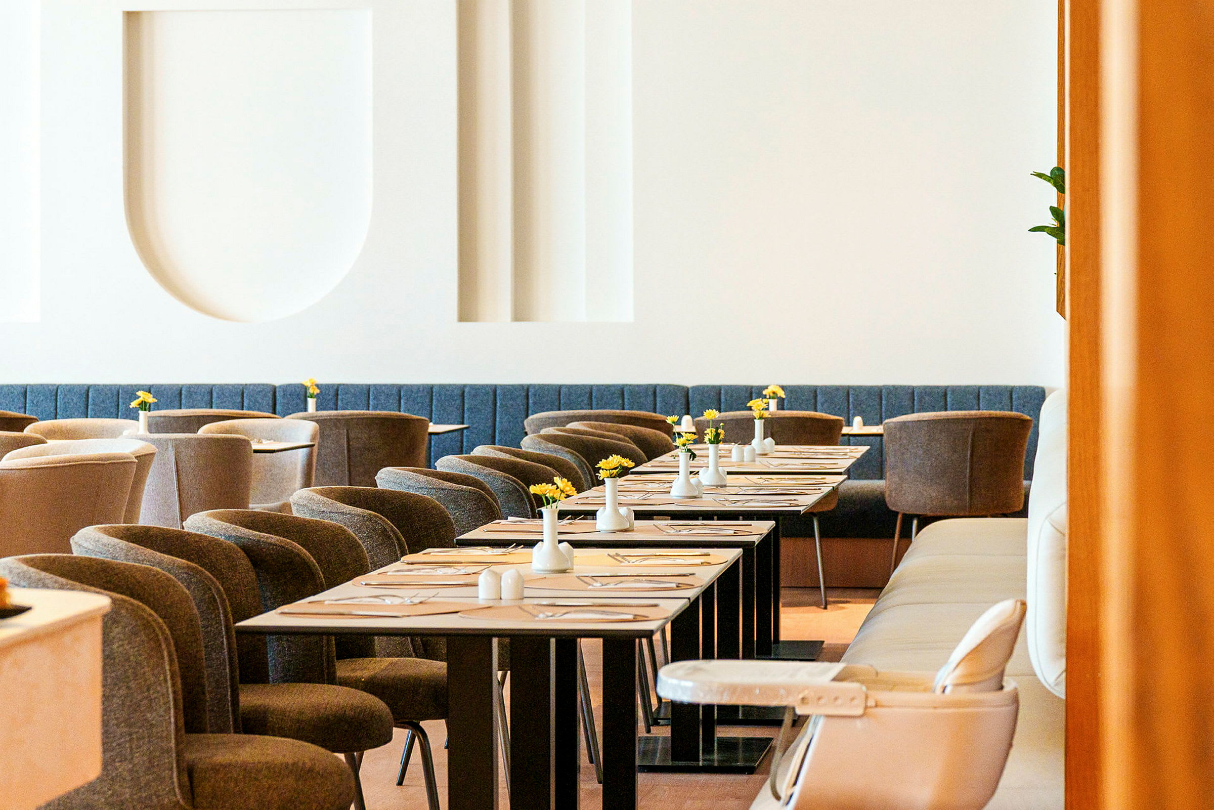 En elegant restaurant med moderne møbler, dekkede bord og små vaser med gule blomster. (AI-generert tekst)