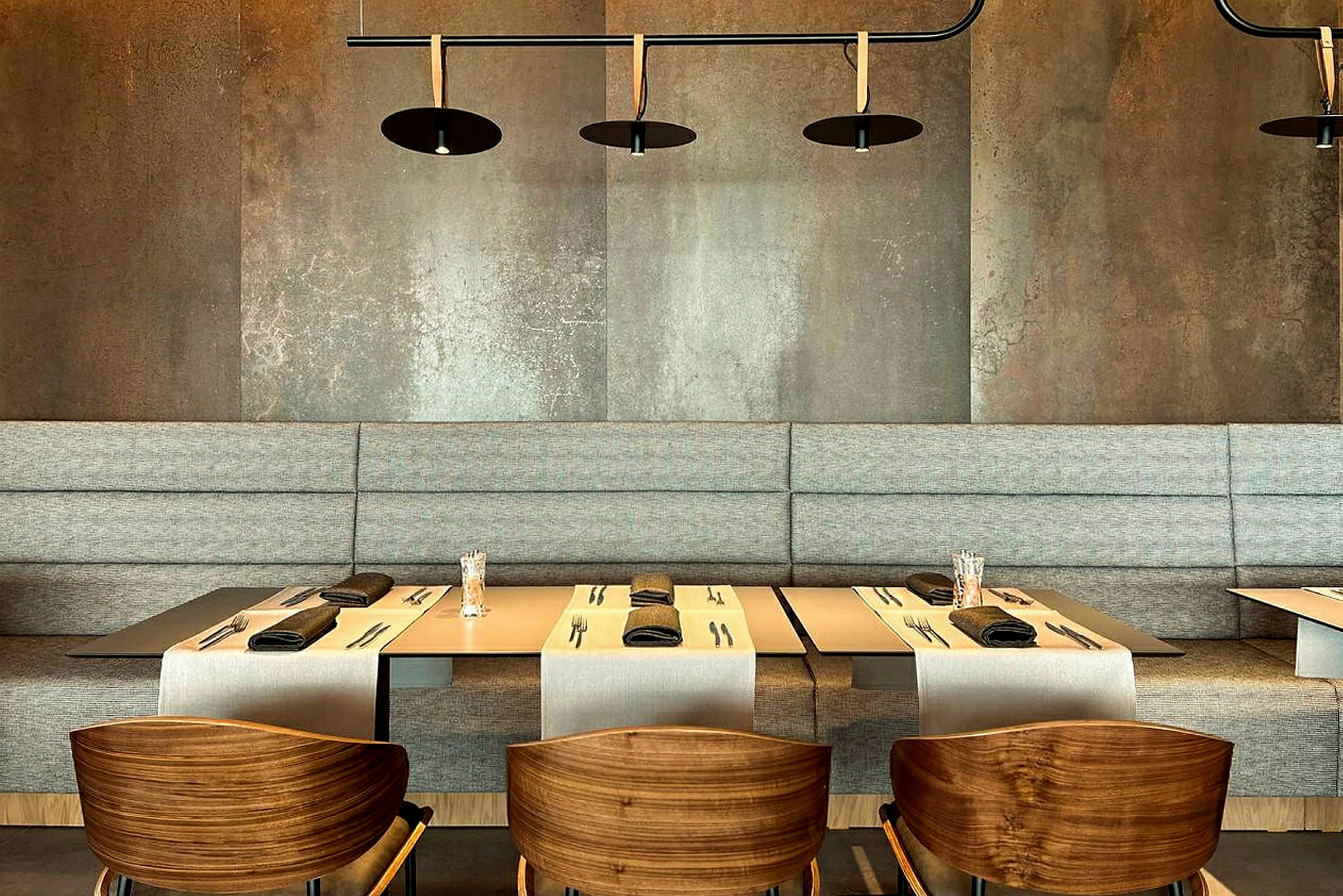 En moderne restaurantinteriør med bord dekket for middag, stoler med treseter og en grå bakgrunn. (AI-generert tekst)