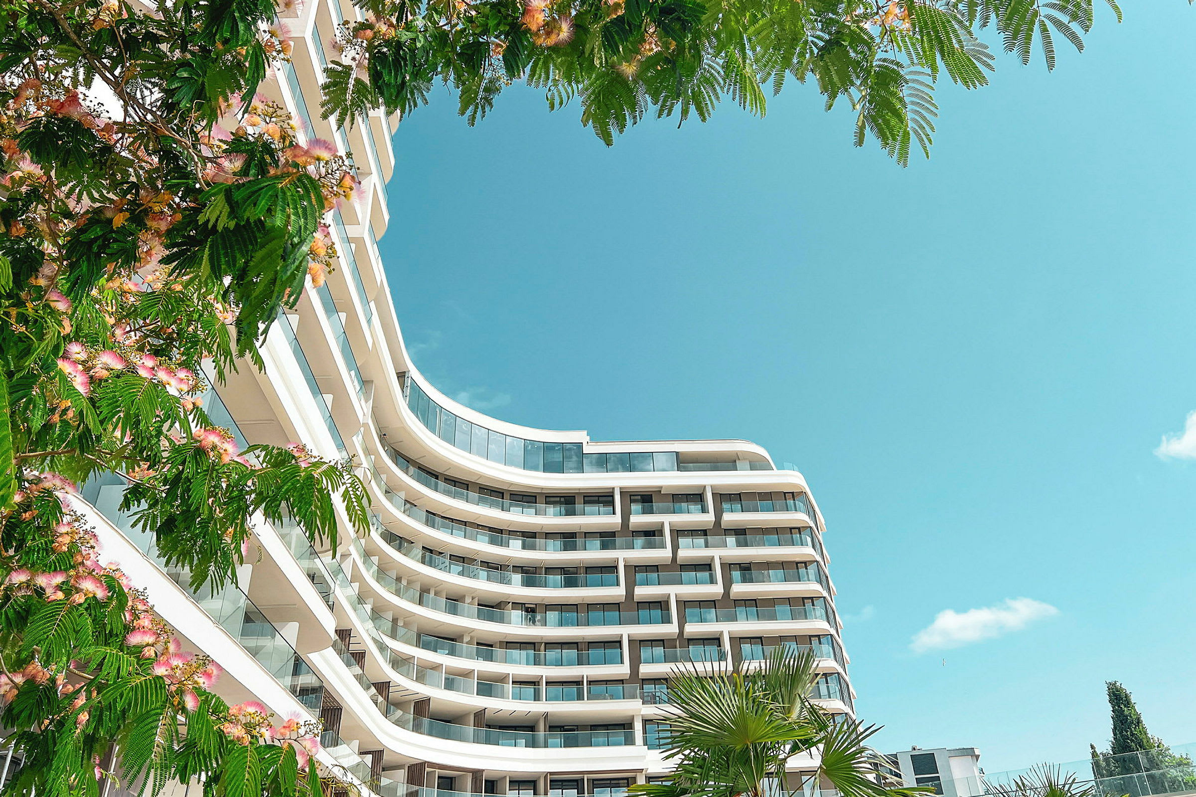 Moderne hotell med balkonger, omgitt av grøntområder og blå himmel. (AI-generert tekst)