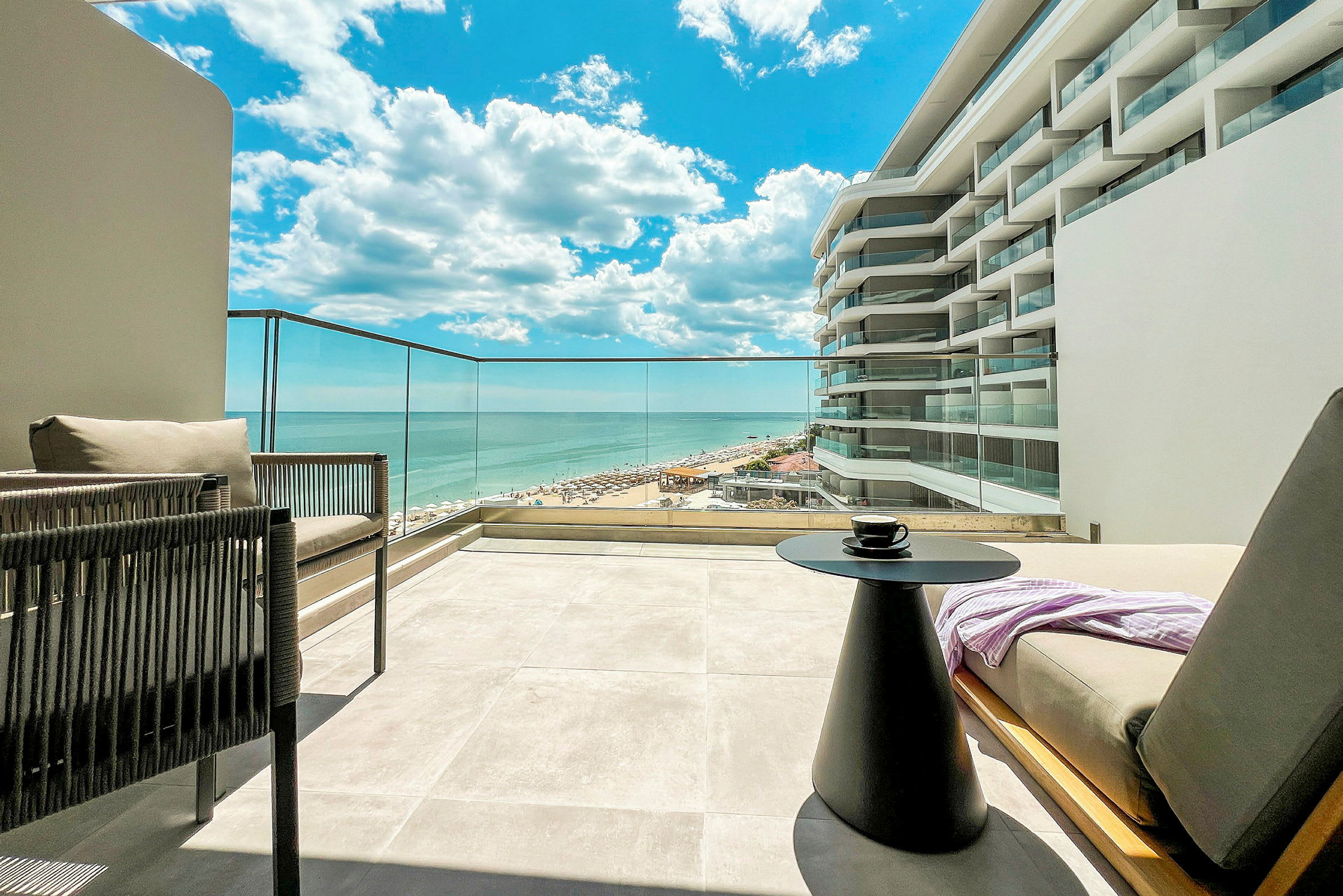 Utsikt fra en terrasse mot havet og en del av en bygning med moderne design. (AI-generert tekst)