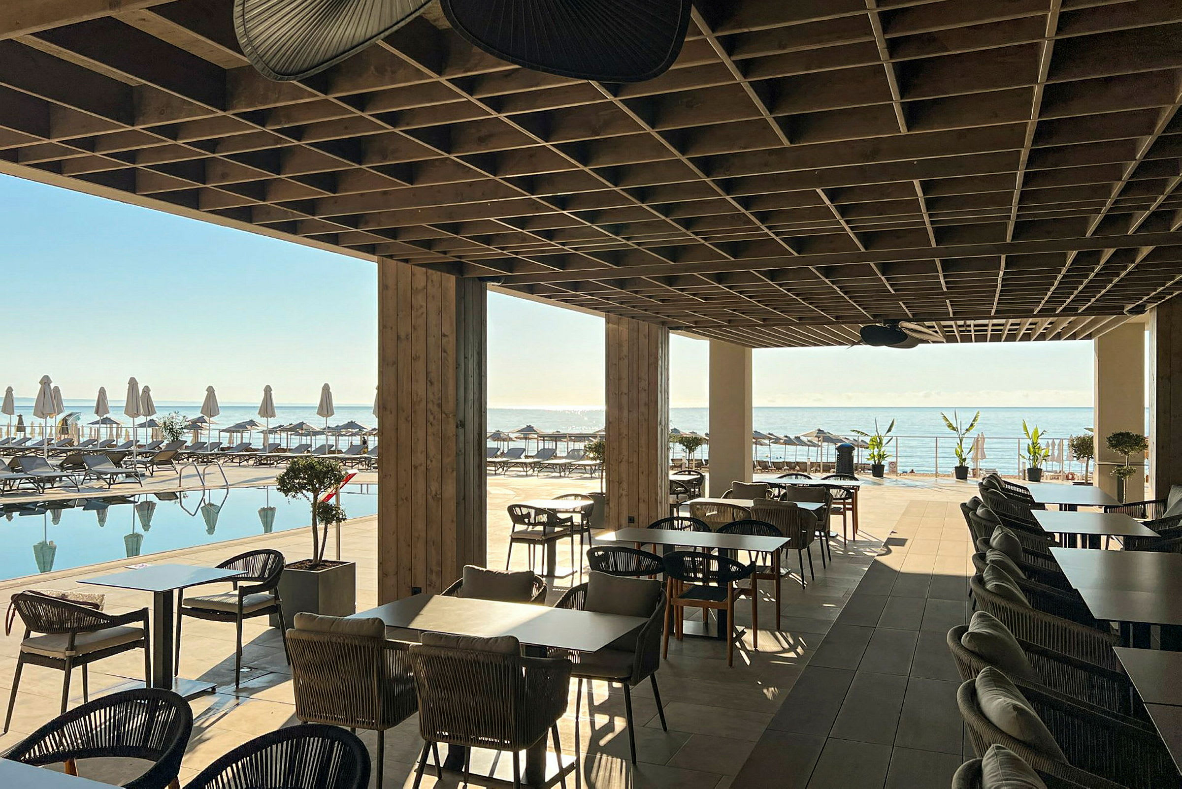 Restaurantområde under tak med utsikt over basseng og hav. (AI-generert tekst)