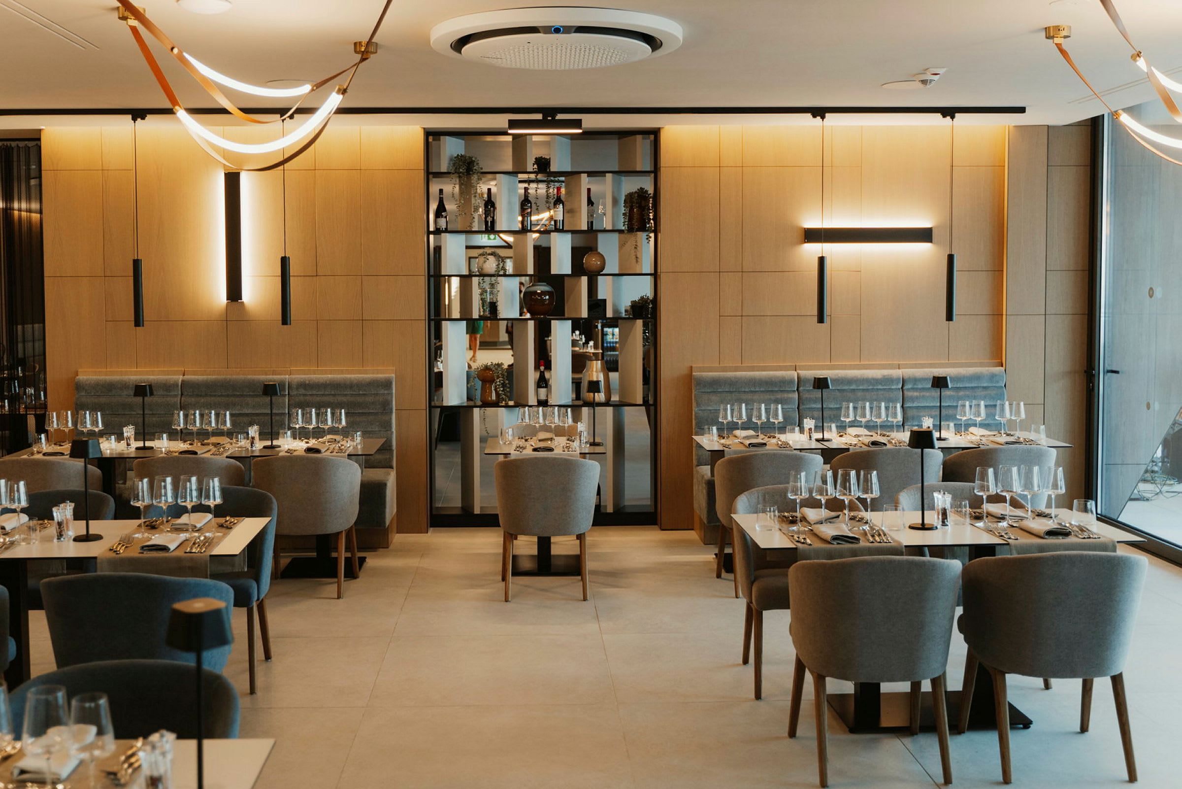 Restaurant med dekkede bord og komfortable stoler, samt dekorative lamper i taket. (AI-generert tekst)