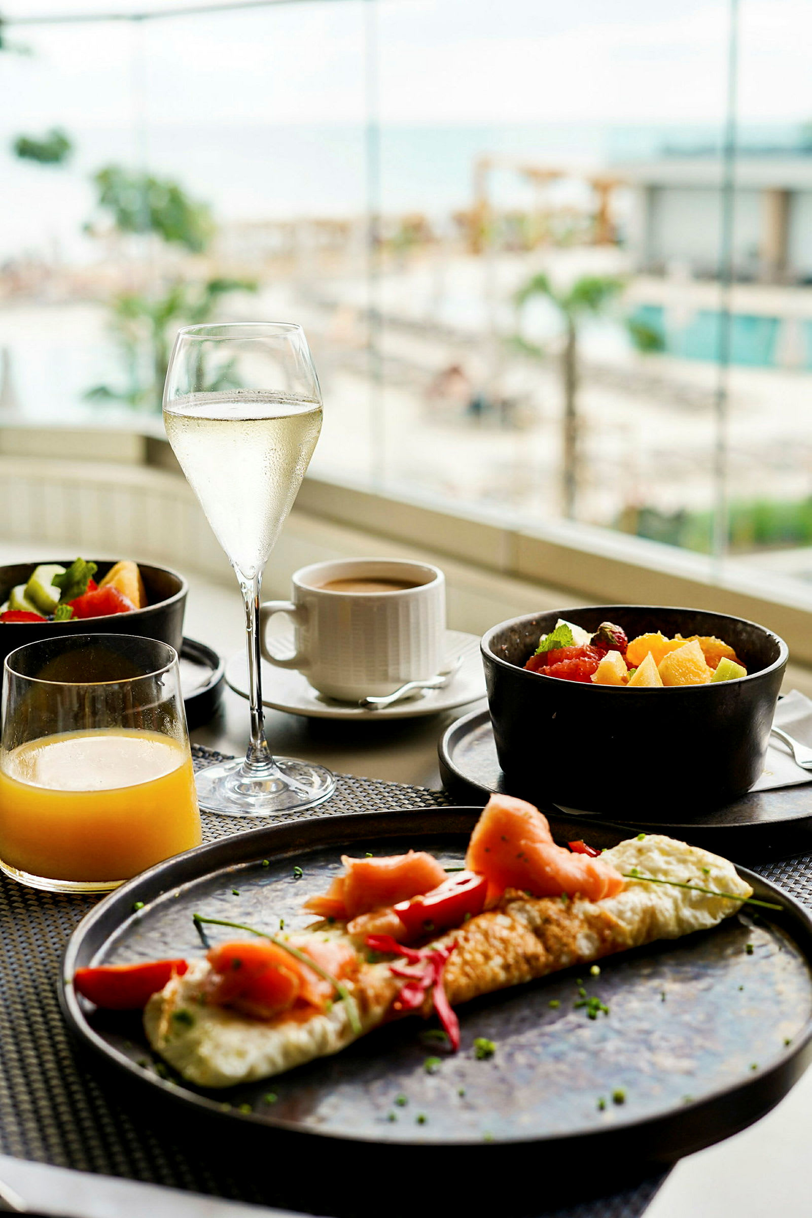 Frokost med omelett, frisk frukt og drikke, med utsikt mot et basseng og havet. (AI-generert tekst)