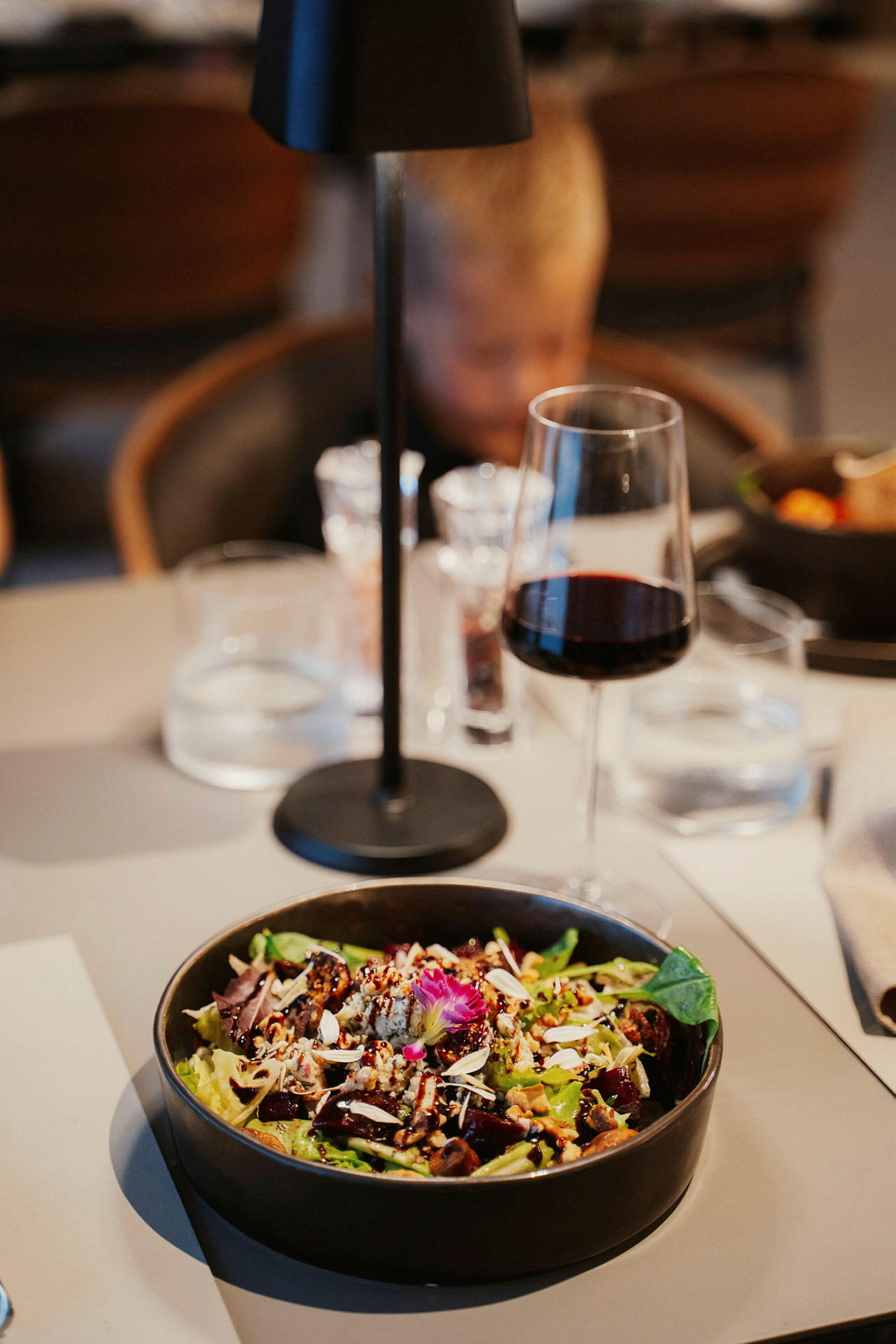 En skål med salat pyntet med nøtter og blomster på et dekket bord. (AI-generert tekst)