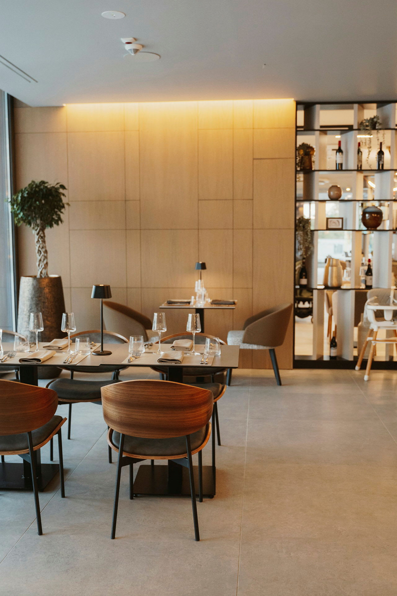 En moderne restaurant med trepaneler, elegante bord og stoler, samt glass og tallerkener klargjort for servering. (AI-generert tekst)