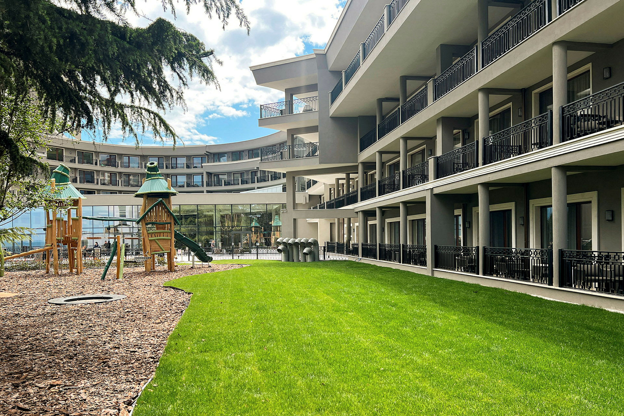Hotellbygning ved grønn gressplen og lekeplass. (AI-generert tekst)
